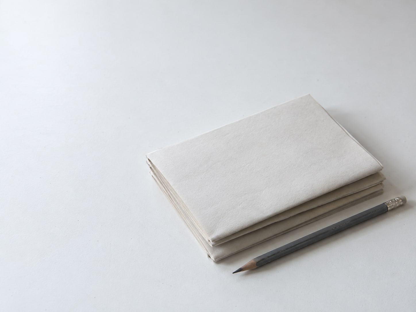 Una pila de hojas en blanco dobladas y un lápiz sobre una mesa blanca limpia.