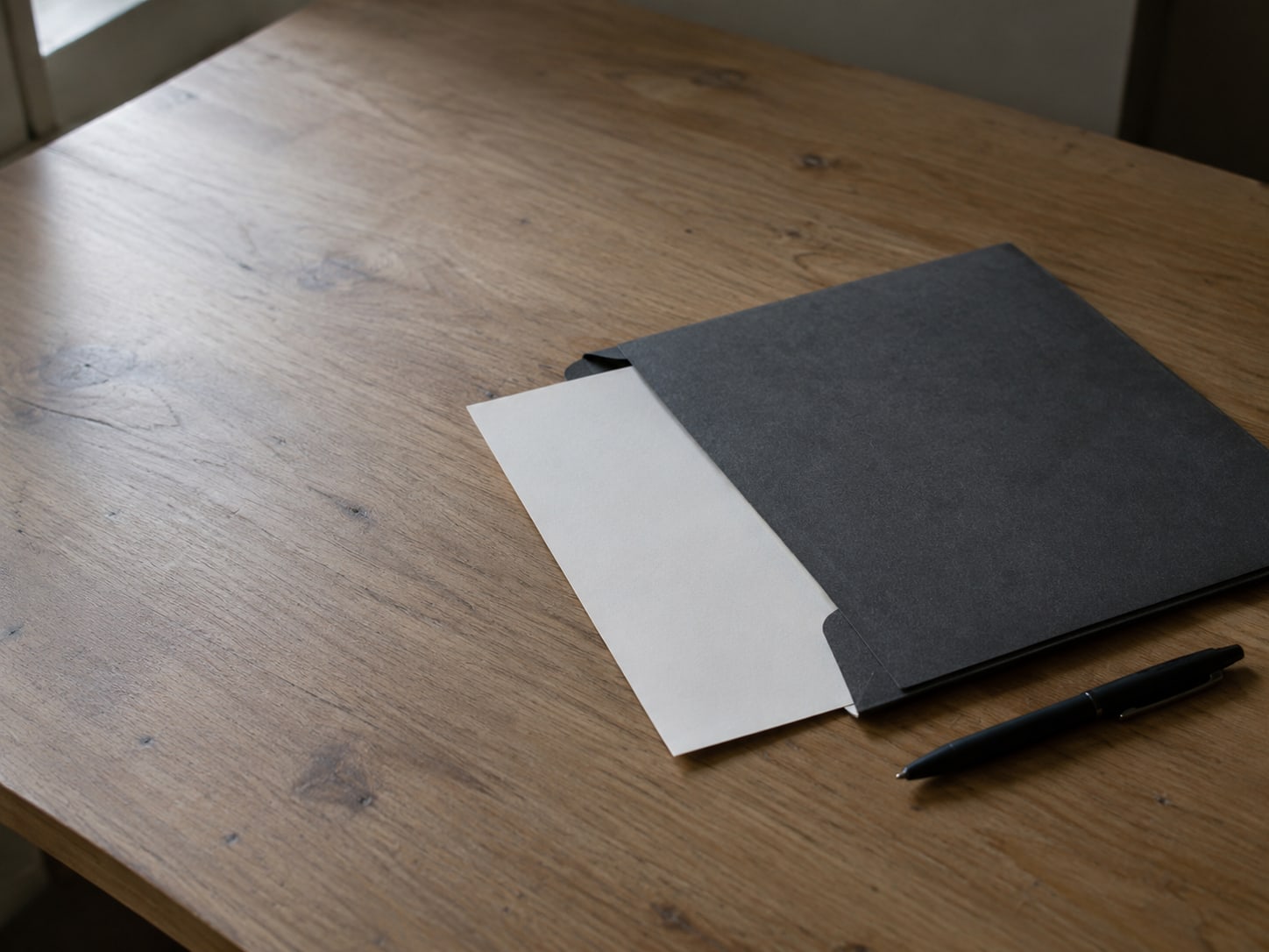 Una carpeta cerrada con una hoja en blanco a medio sacar, junto a una pluma sobre un escritorio.