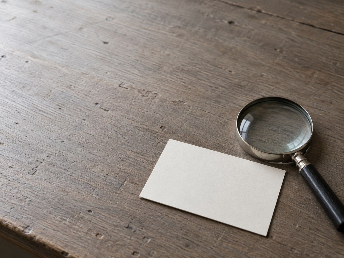 A magnifying glass resting beside a single blank index card on a bare desk.