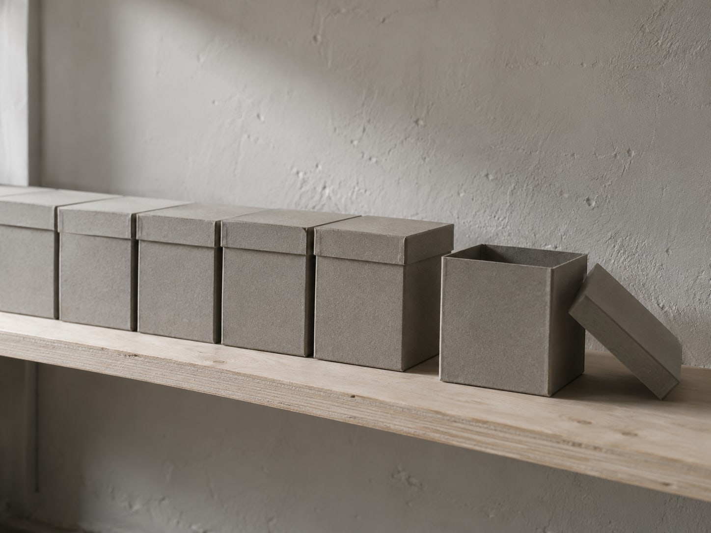 A neat row of identical gray boxes on a shelf with one box set slightly apart and the lid removed.