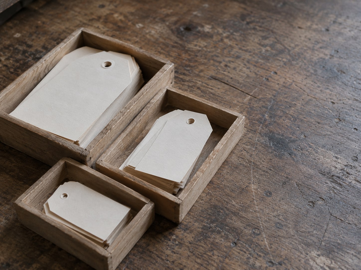 Una pequeña pila de etiquetas de papel en blanco ordenadas en bandejas de madera separadas, sobre un banco de trabajo.