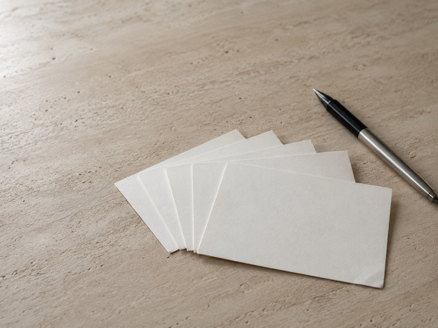 Five blank index cards fanned out beside a pen on a plain table, one card turned slightly toward the viewer.