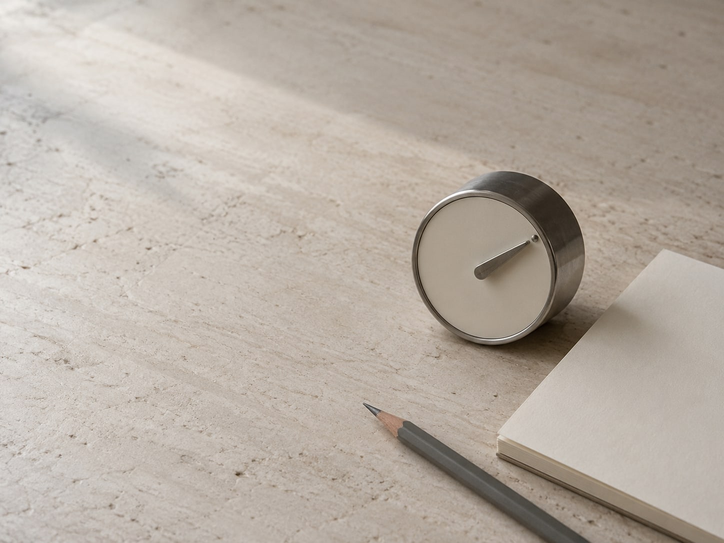 A kitchen timer set to ten minutes next to a blank notepad and a pencil on a clean table.