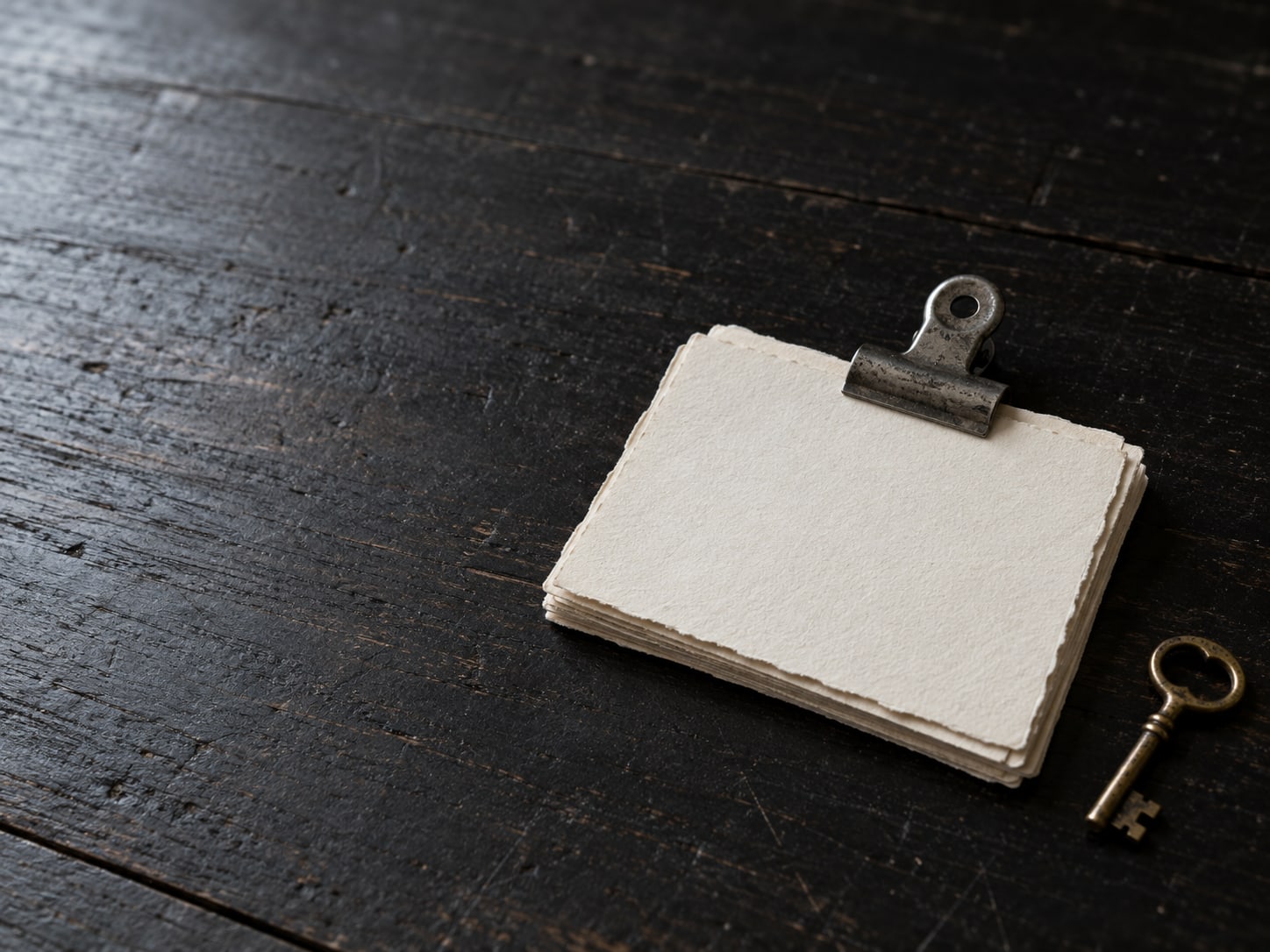 A stack of paper cards held with a metal clip next to a small brass key on a dark table.
