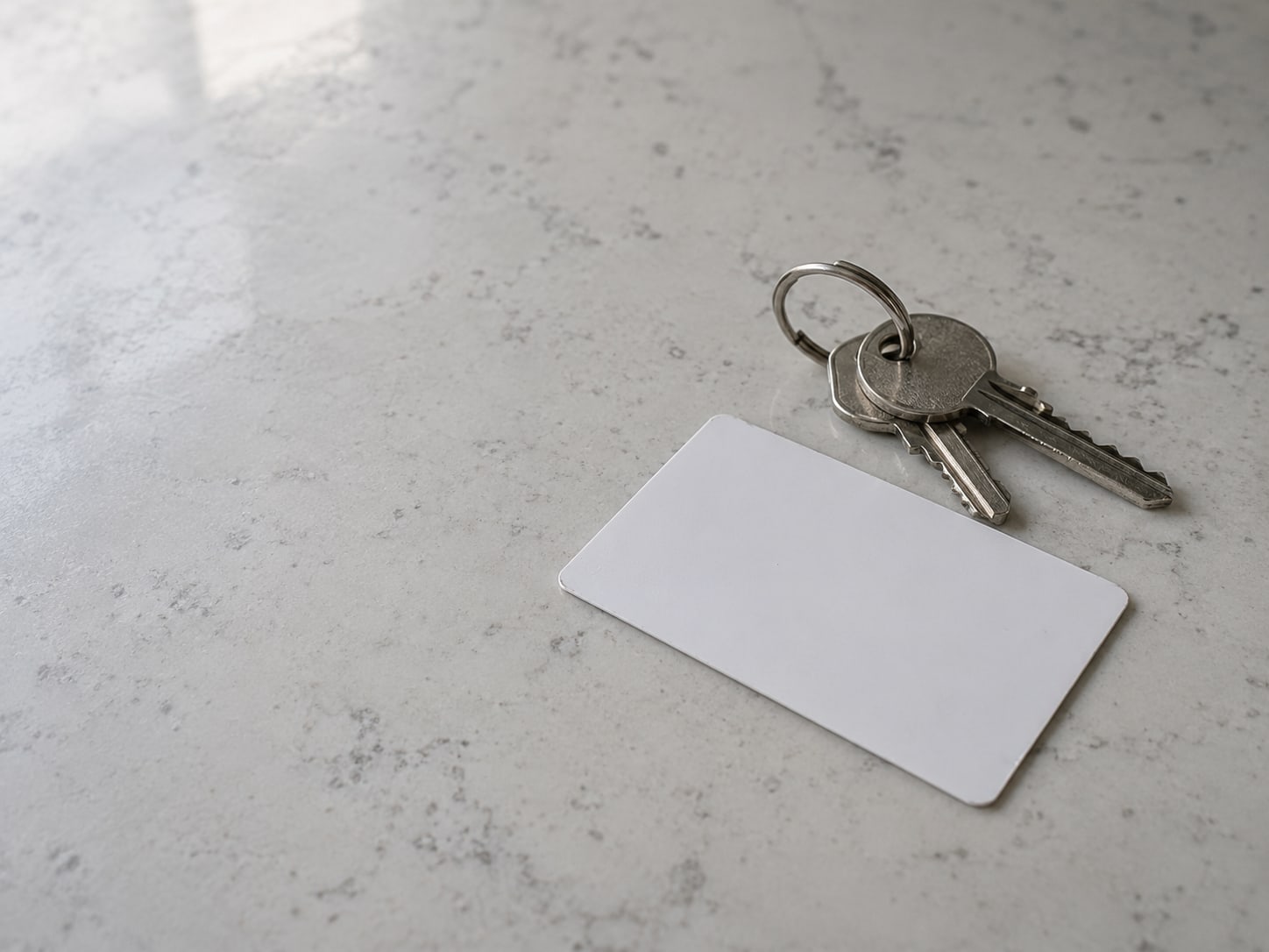 Un llavero con llaves de casa y una tarjeta blanca en blanco sobre una cocina limpia después de una visita terminada.