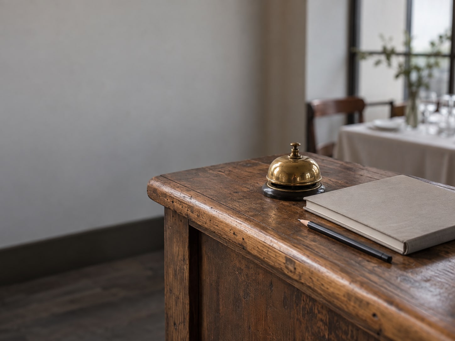 A brass service bell on a wooden host stand beside a closed reservation book and a pencil.