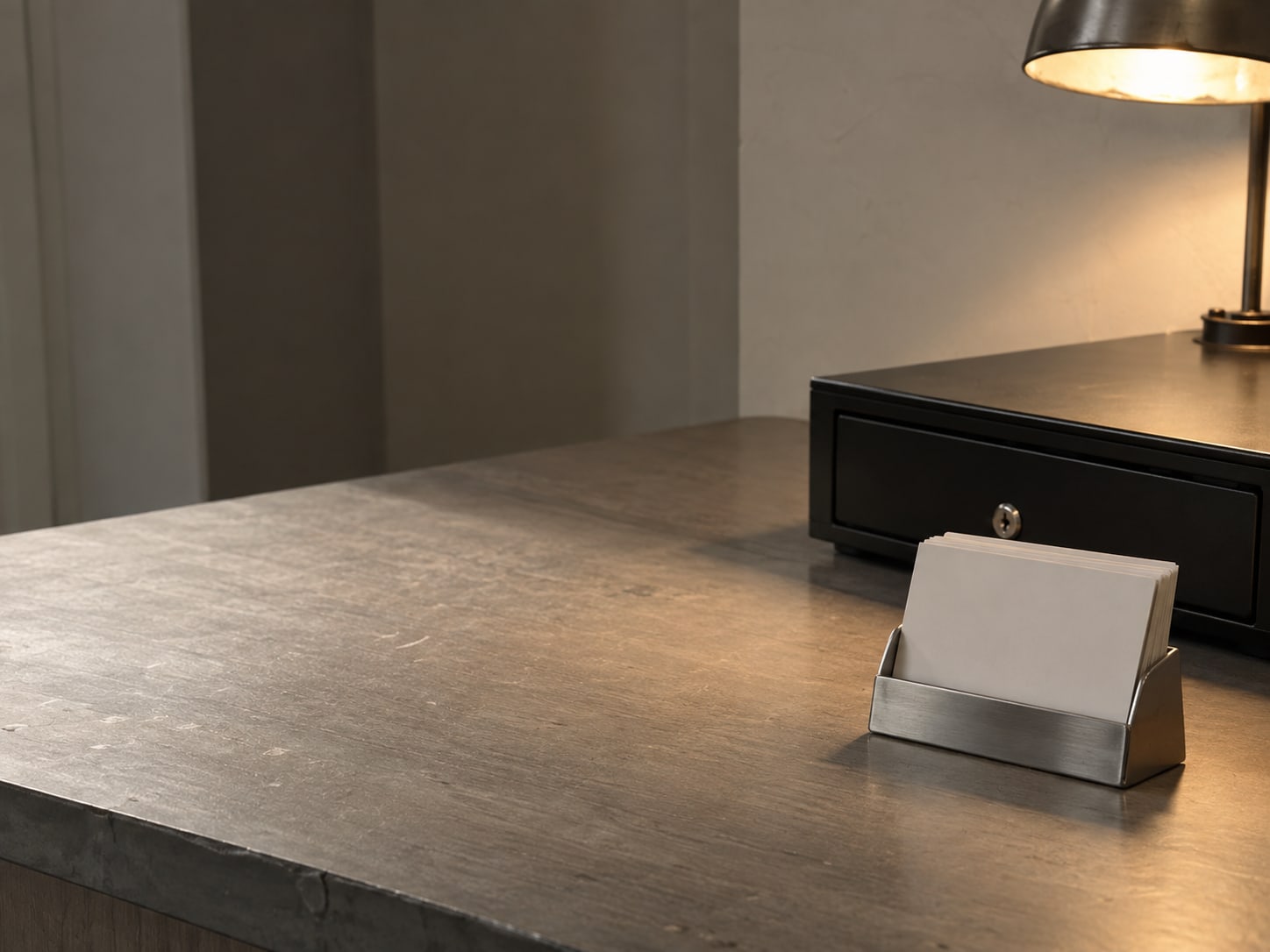 A small stand holding blank cards near a closed cash drawer on a salon front desk, lit by a warm lamp.