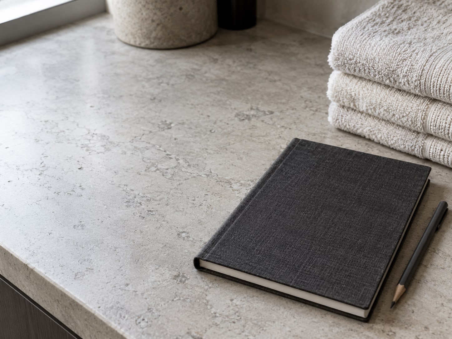 A closed notebook and a pencil on a styling counter next to a stack of folded towels in a quiet salon.