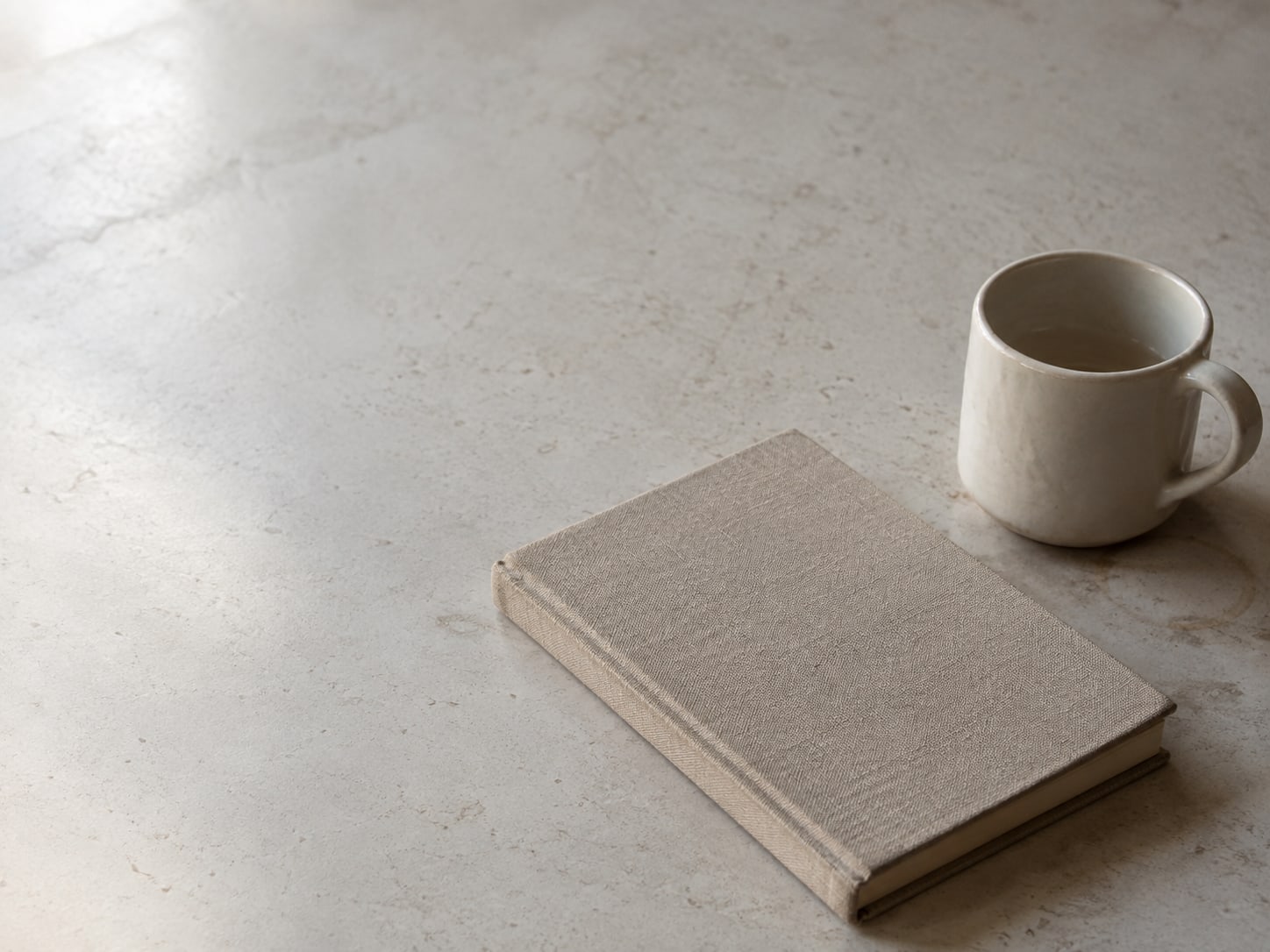 Una agenda de citas cerrada y una taza de cerámica sobre un mostrador a la luz de la mañana.