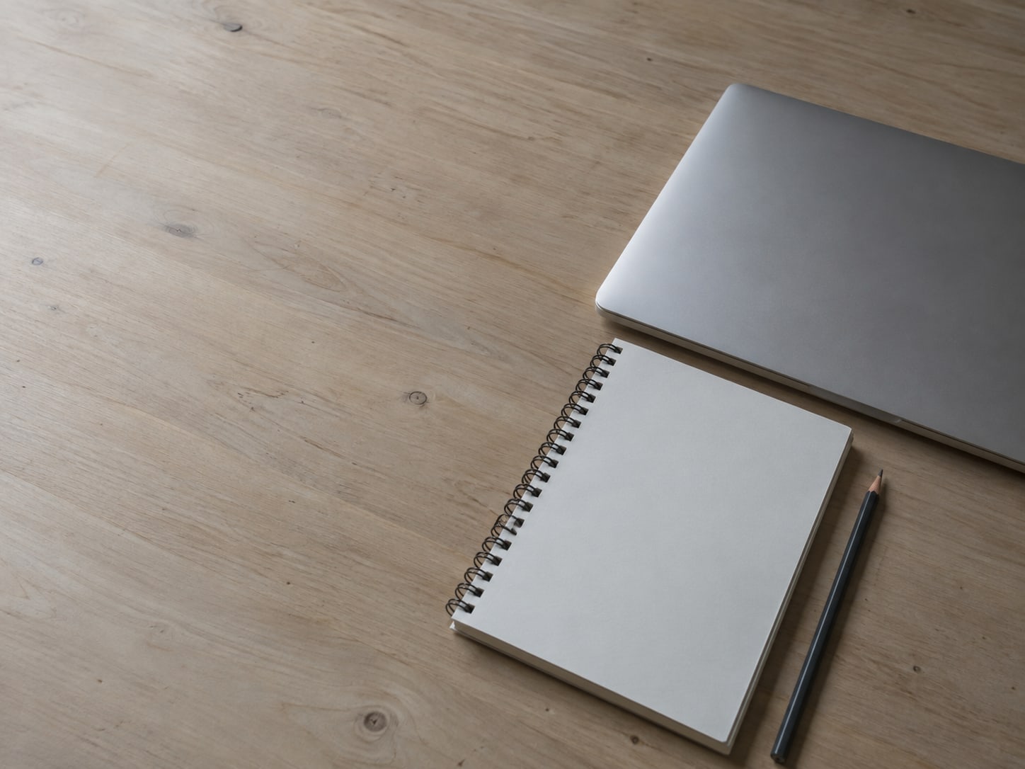 Un bloc de notas en blanco y un lápiz junto a una laptop cerrada sobre un escritorio de madera.