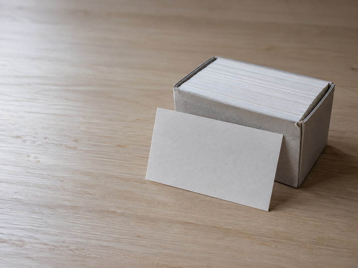 Una caja pequeña de fichas en blanco con una ficha asomando hacia adelante sobre un escritorio ordenado.