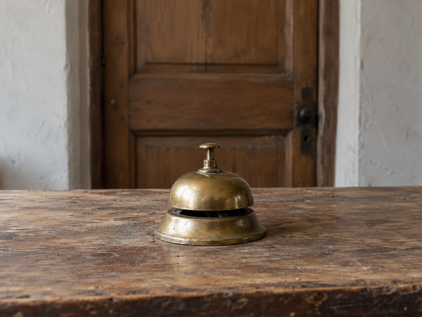 A single small brass bell on a plain wooden shop counter, with the door behind it closed.