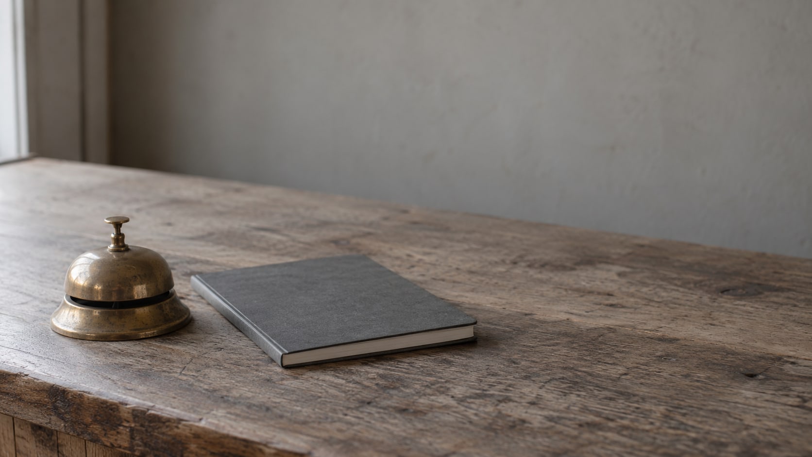 A small brass bell on a plain wooden shop counter beside a closed notebook.