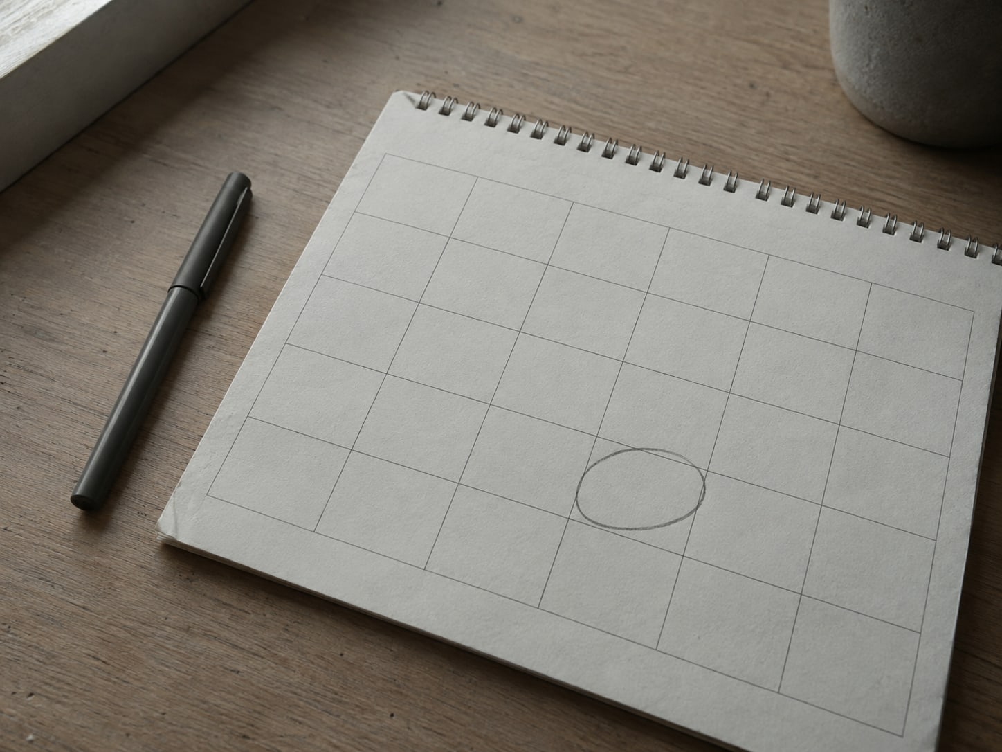 A paper calendar on a desk with one date circled in pencil, a closed pen resting beside it.