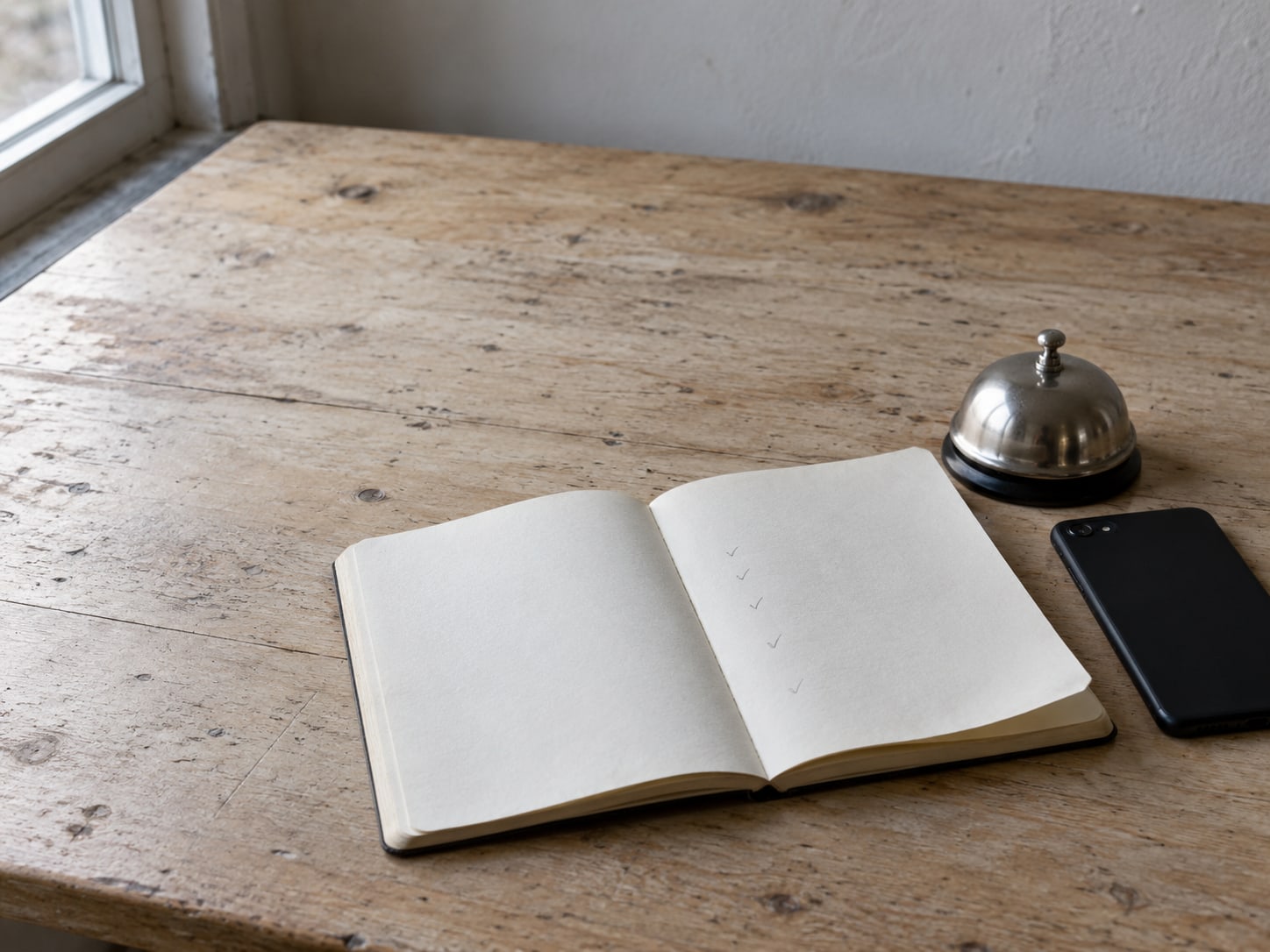 A notebook open to a page of pencil tick marks beside a small desk bell and a closed phone.