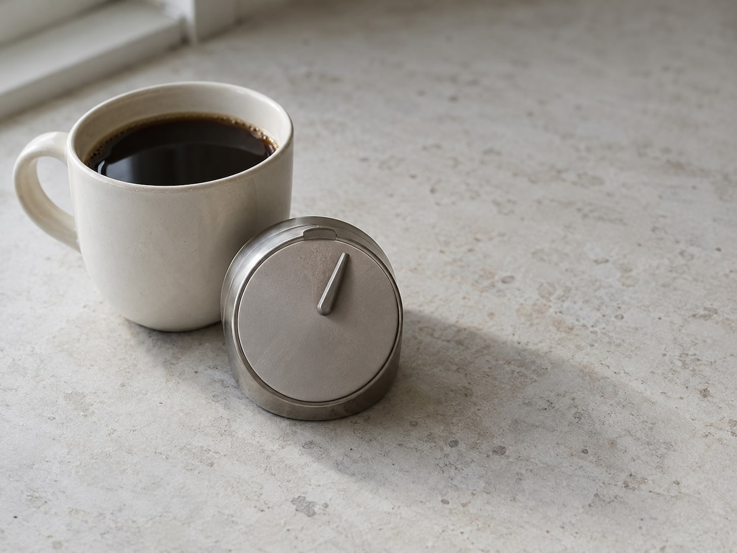 A small kitchen timer set to a few minutes beside a cup of coffee on a clean counter.