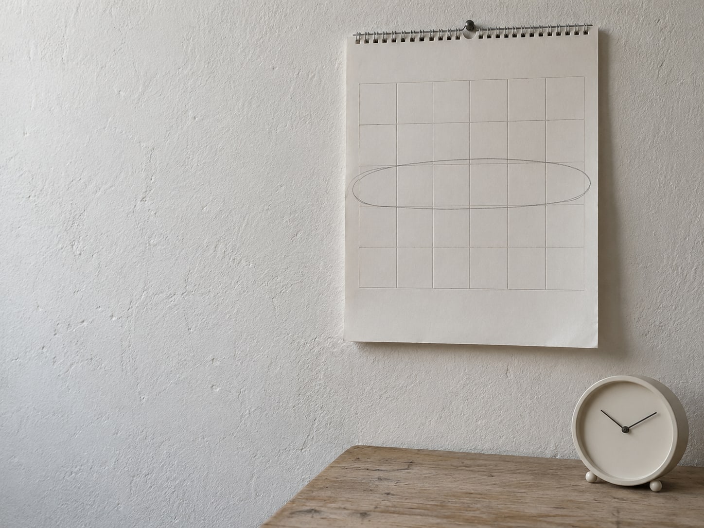 Una hoja de calendario de pared con una sola semana encerrada a lápiz y un pequeño reloj de escritorio al lado.