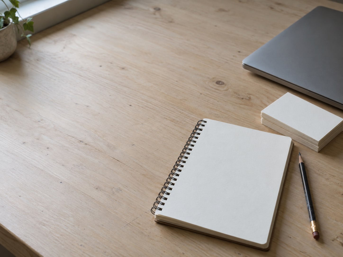 A notepad and a pencil beside a closed laptop on a clean desk, with a small stack of blank index cards.