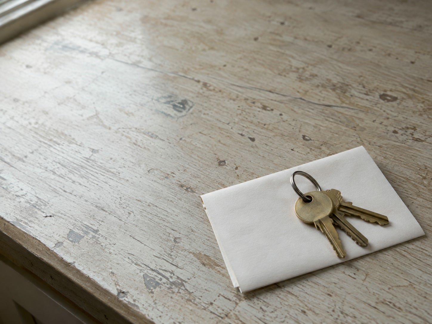 Un llavero de llaves de latón liso descansando sobre una hoja de papel en blanco doblada en un mostrador de madera.