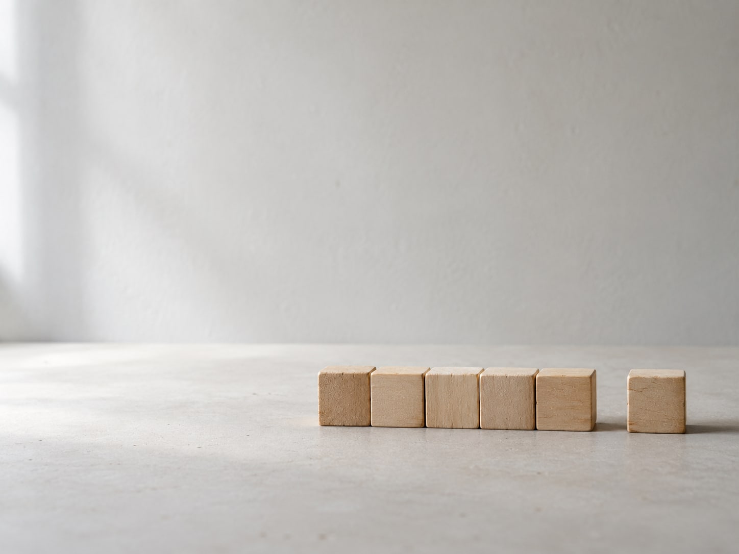 Six small wooden blocks lined up in a row on a pale tabletop, one slightly apart from the others.