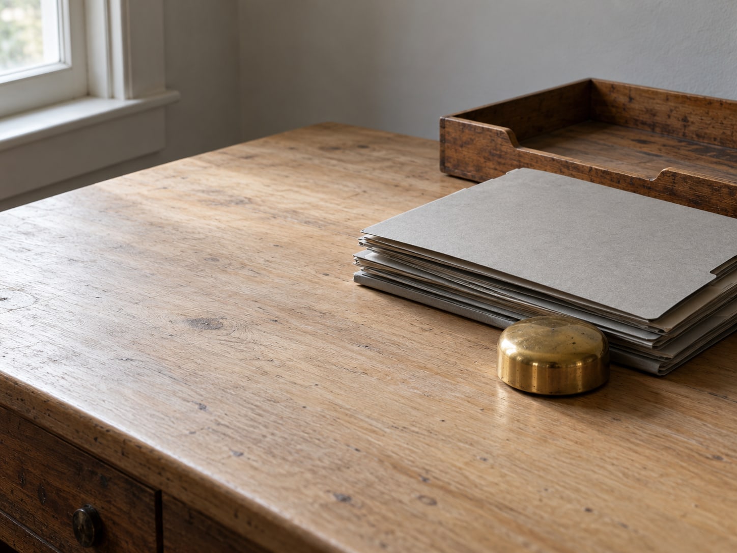 A stack of closed folders beside a brass paperweight and an empty desk tray.
