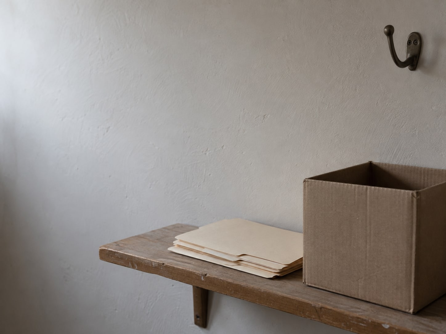 A stack of blank folders and an empty cardboard box on a shelf beside a coat hook.