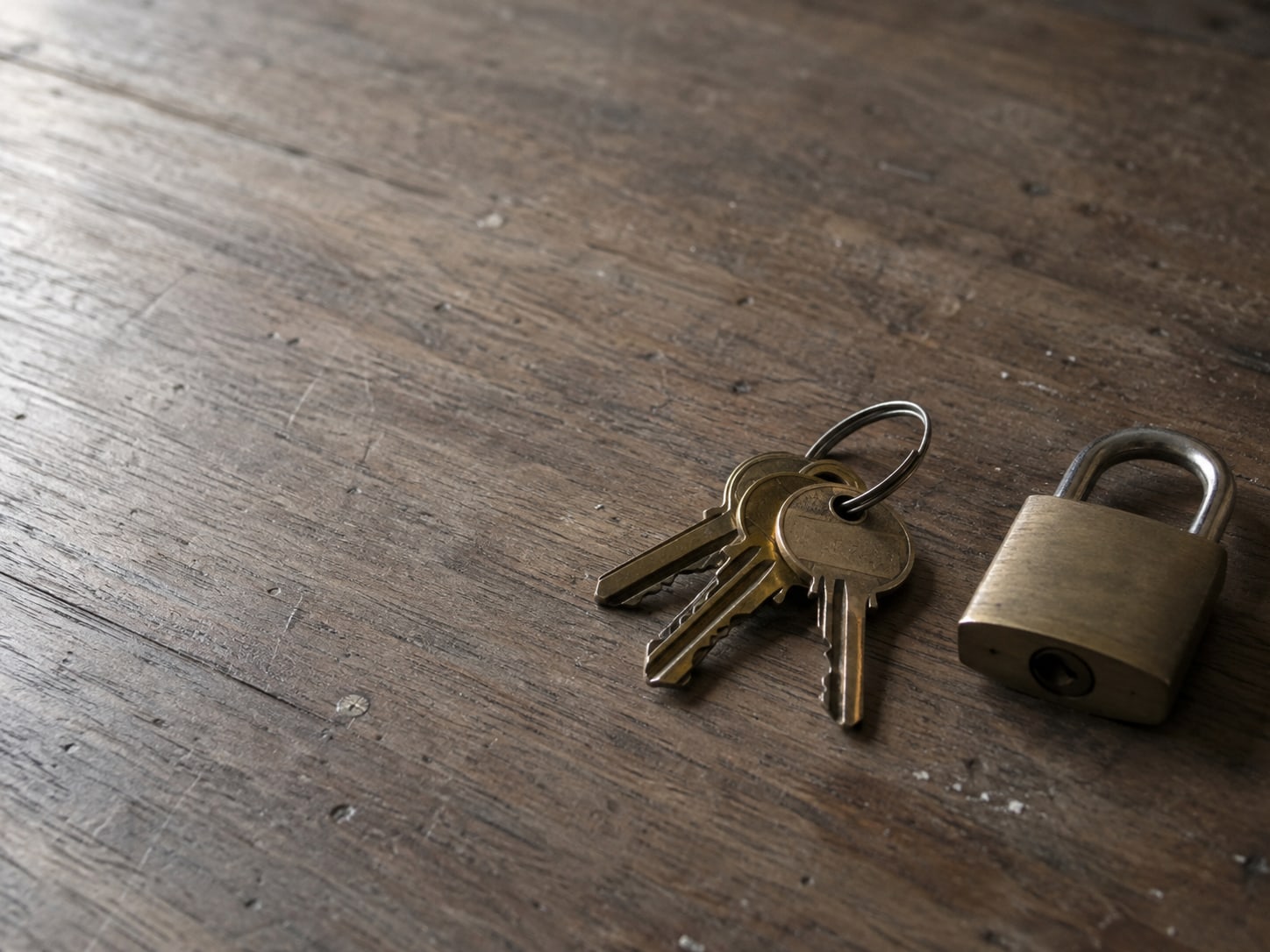 A ring of brass keys on a wooden table beside a small closed padlock.