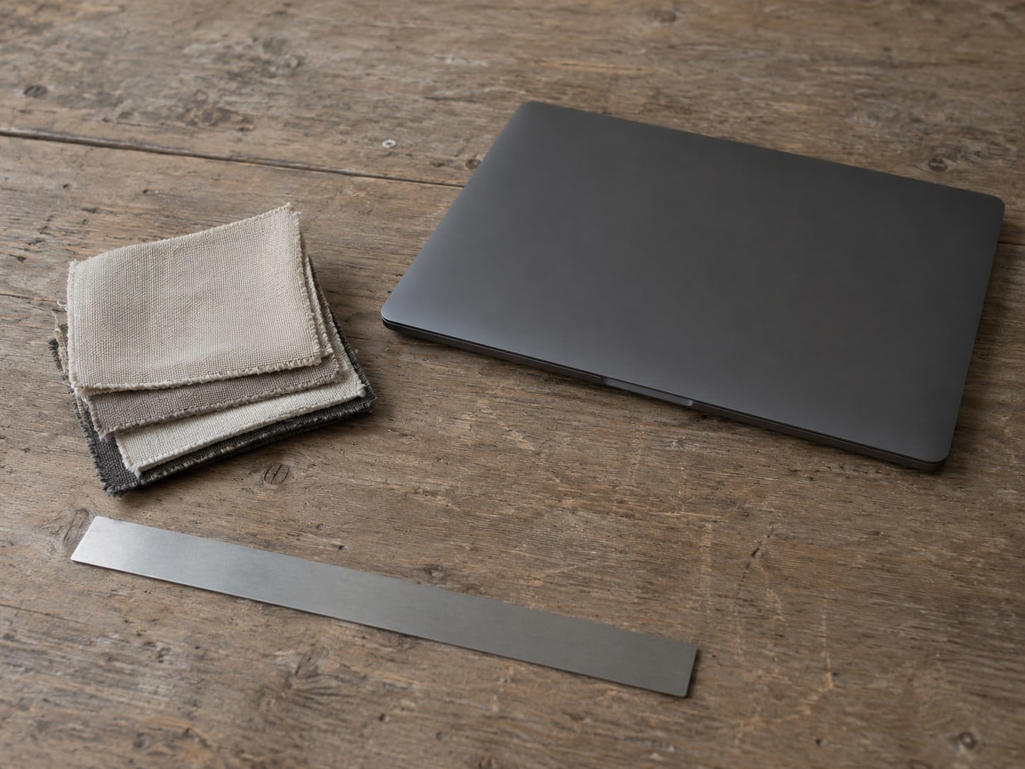 A closed laptop beside a small stack of fabric swatches and a ruler on a worn wooden desk.