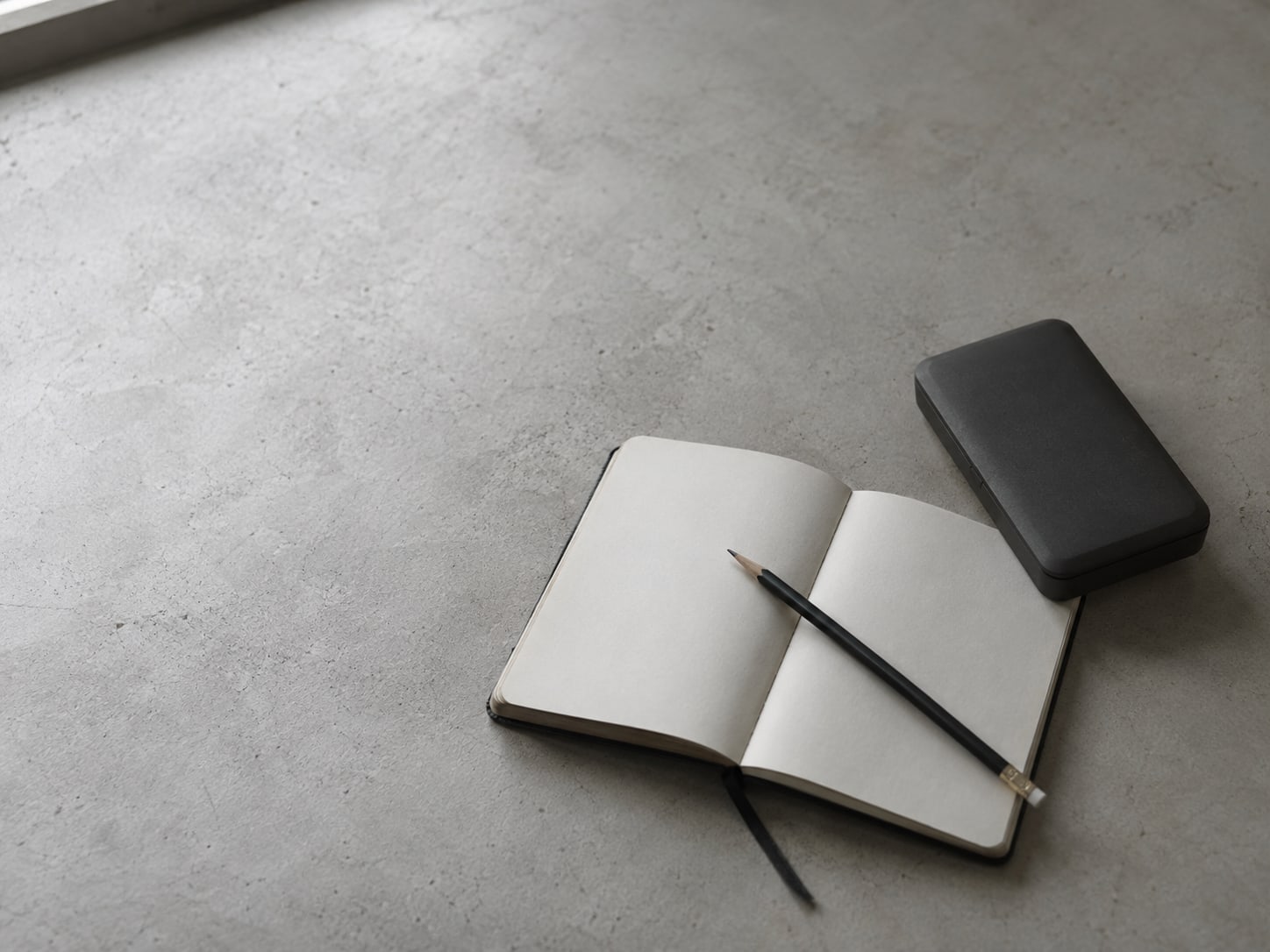 A small ledger book with a pencil resting across it next to a closed calculator on a plain desk.