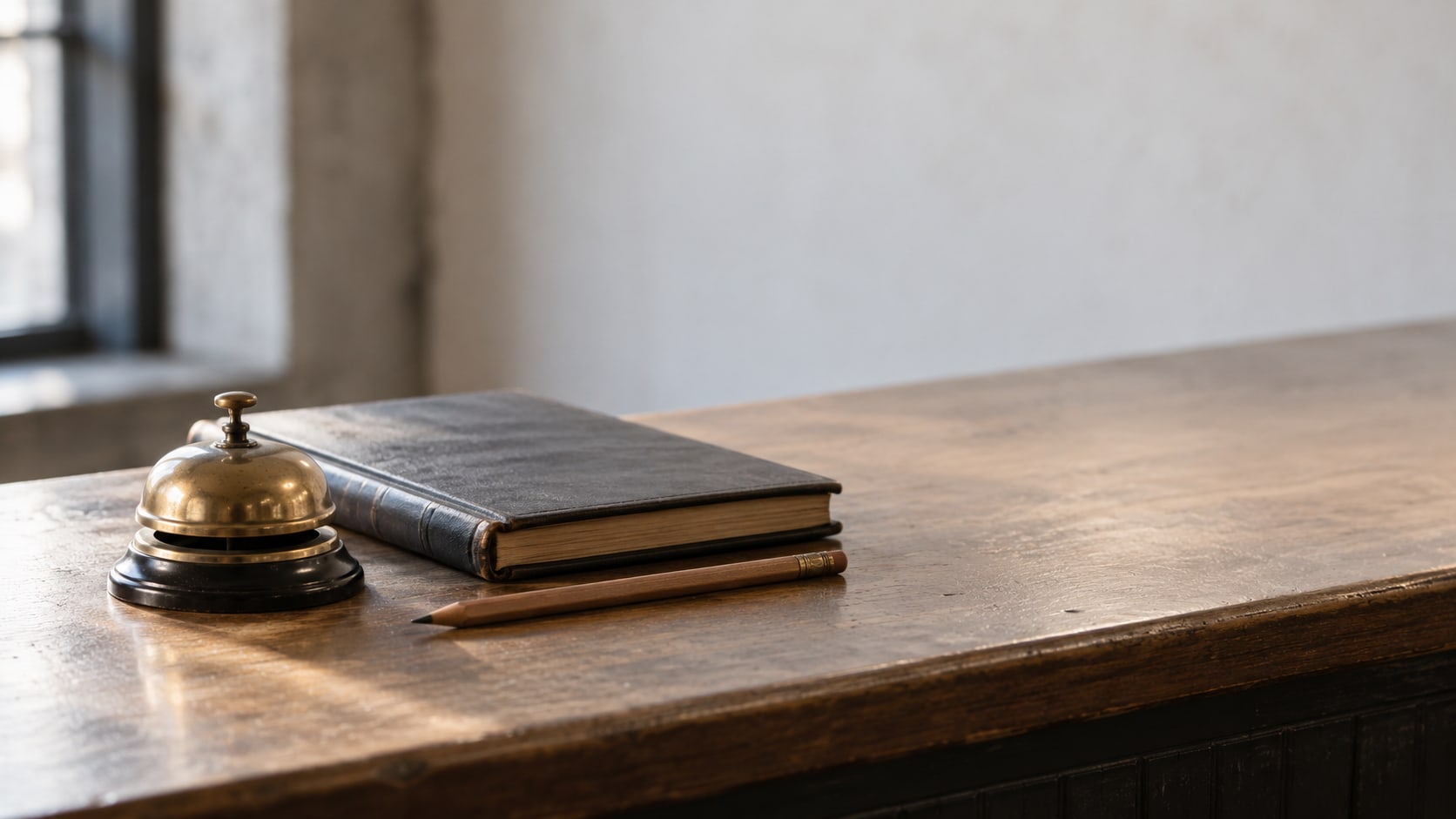 A small brass service bell on a wooden shop counter beside a closed ledger and a pencil.