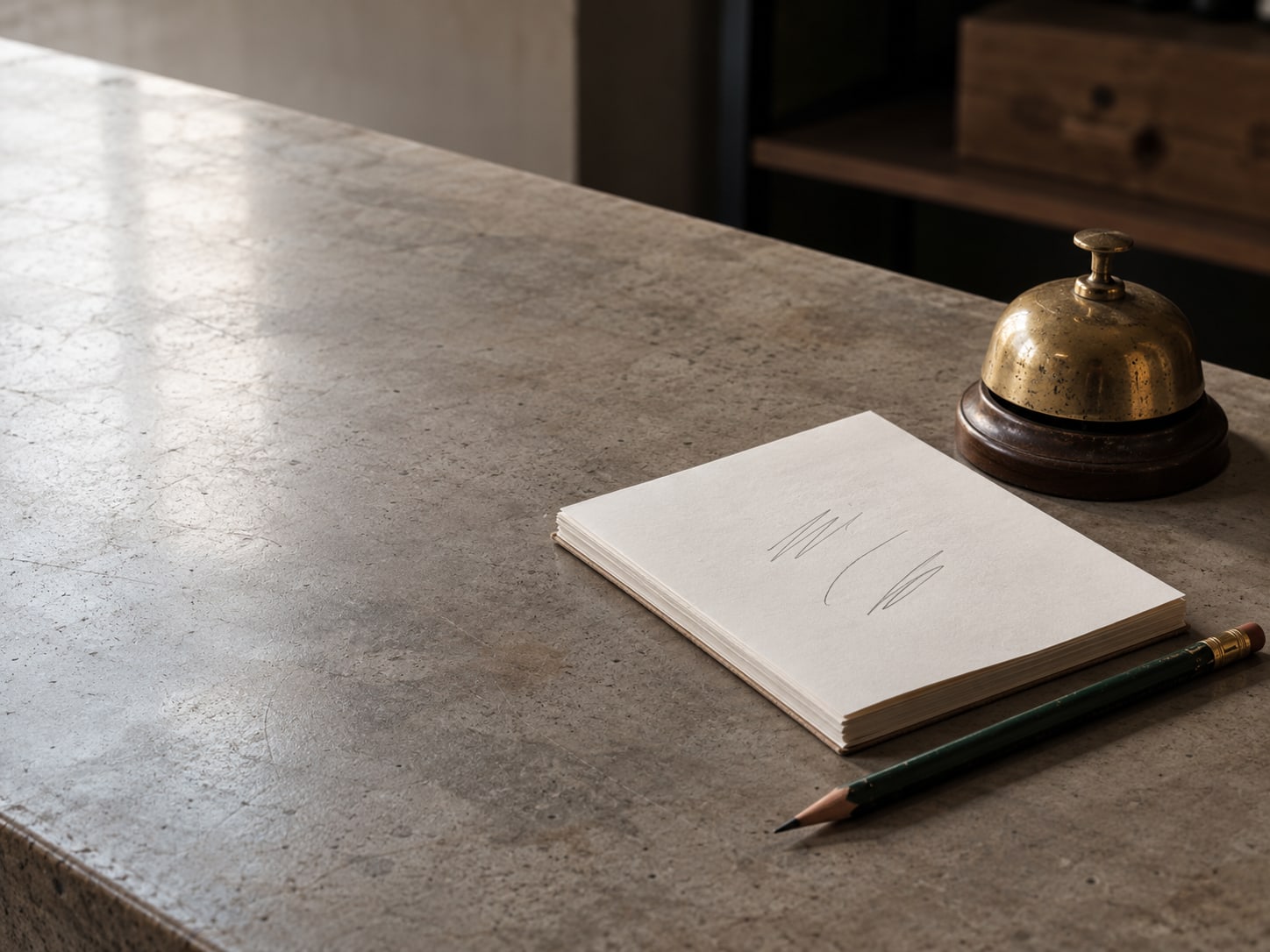A notepad with a few pencil lines on it, a pencil and a small brass bell on a shop counter.