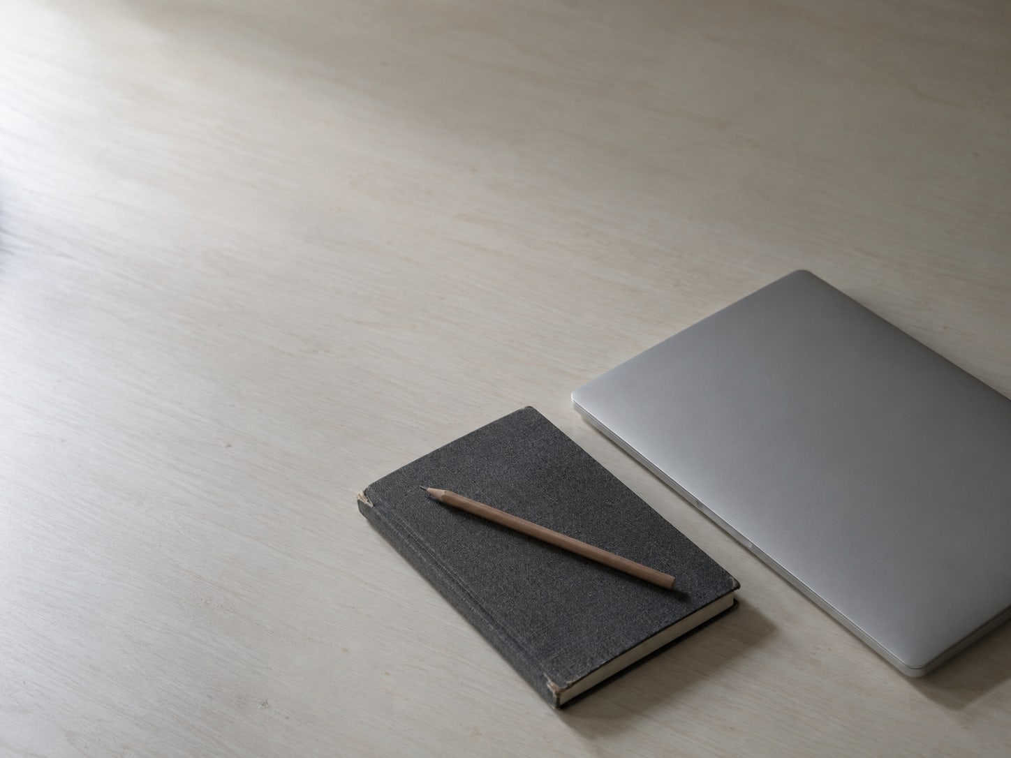 A closed notebook with a pencil on top, next to a switched-off laptop on a clean desk.