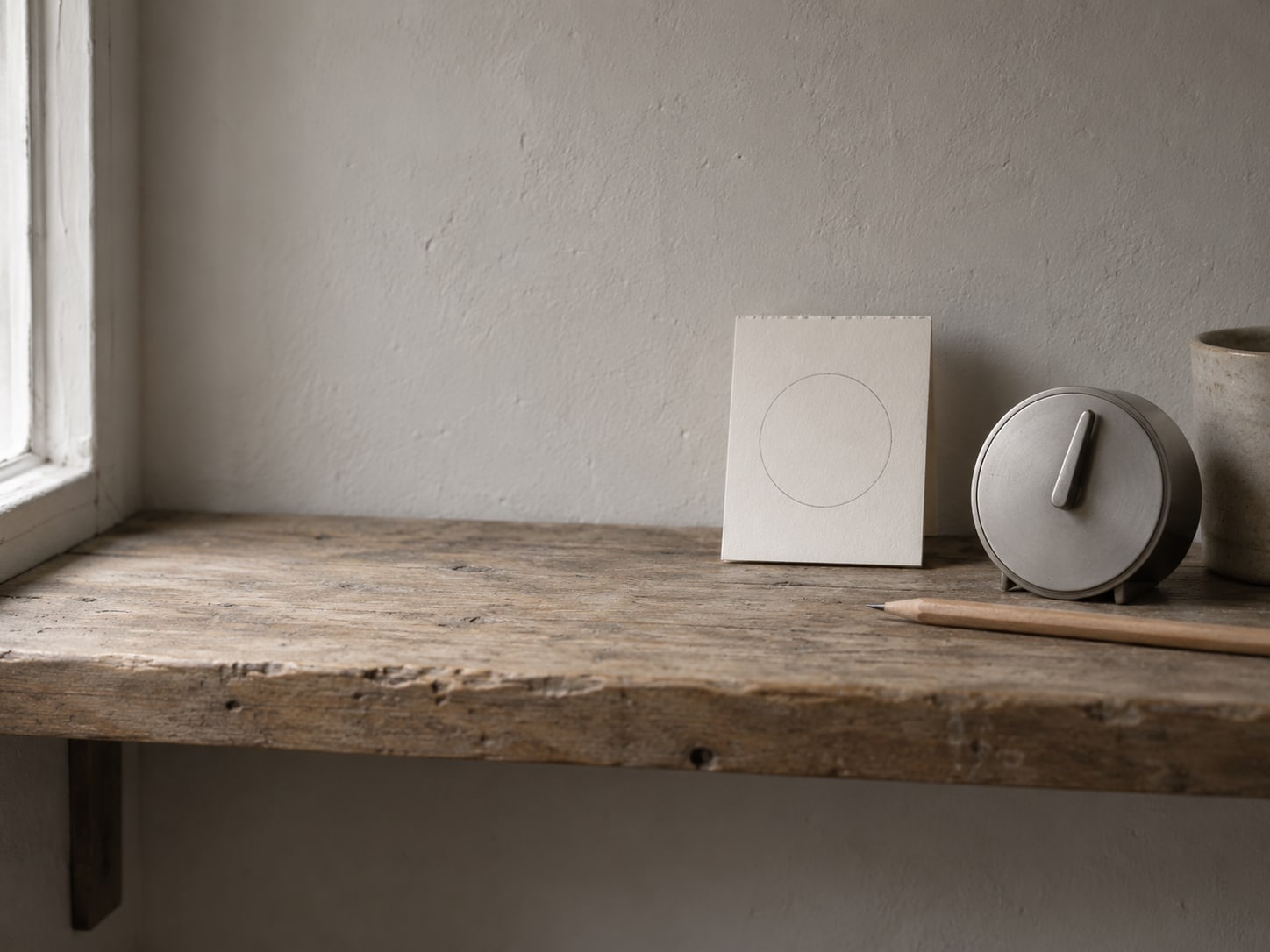 Una pequeña página de calendario con una sola semana marcada con lápiz junto a un sencillo temporizador de cocina sobre un estante de madera.