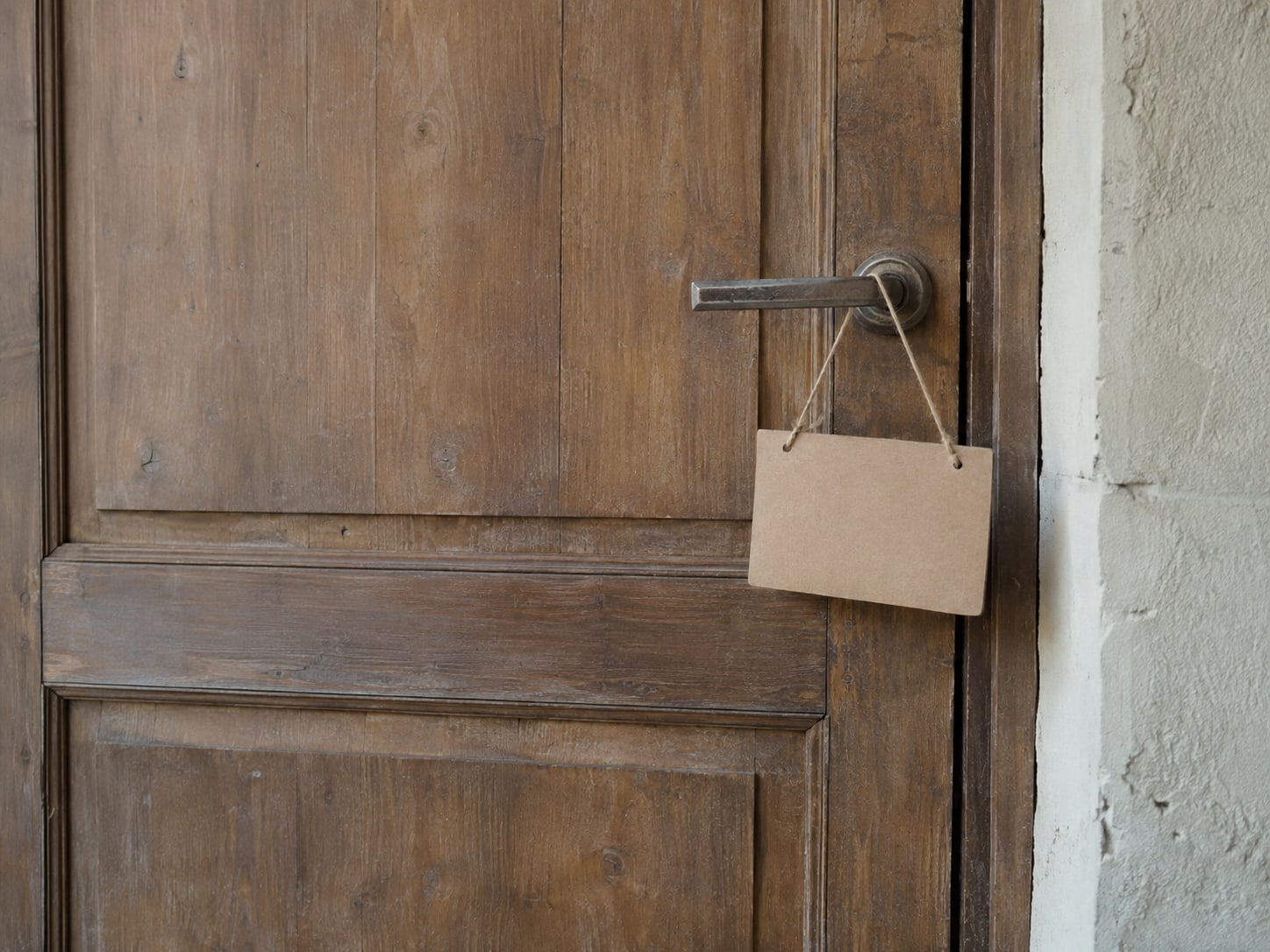 A plain wooden shop door with a blank cardboard sign hanging from the handle.