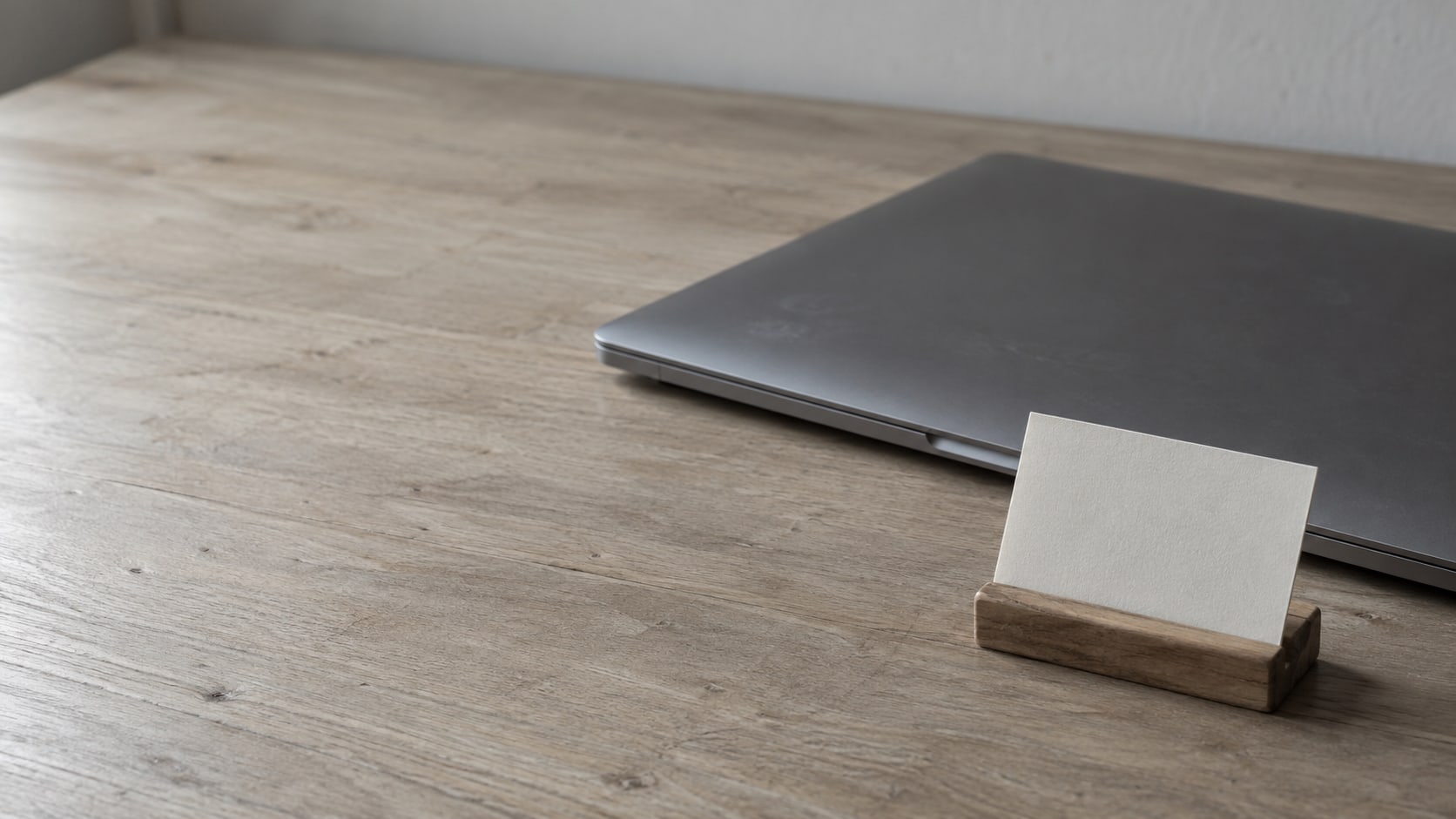 A closed laptop beside a small wooden nameplate stand holding a blank card on a clean desk.