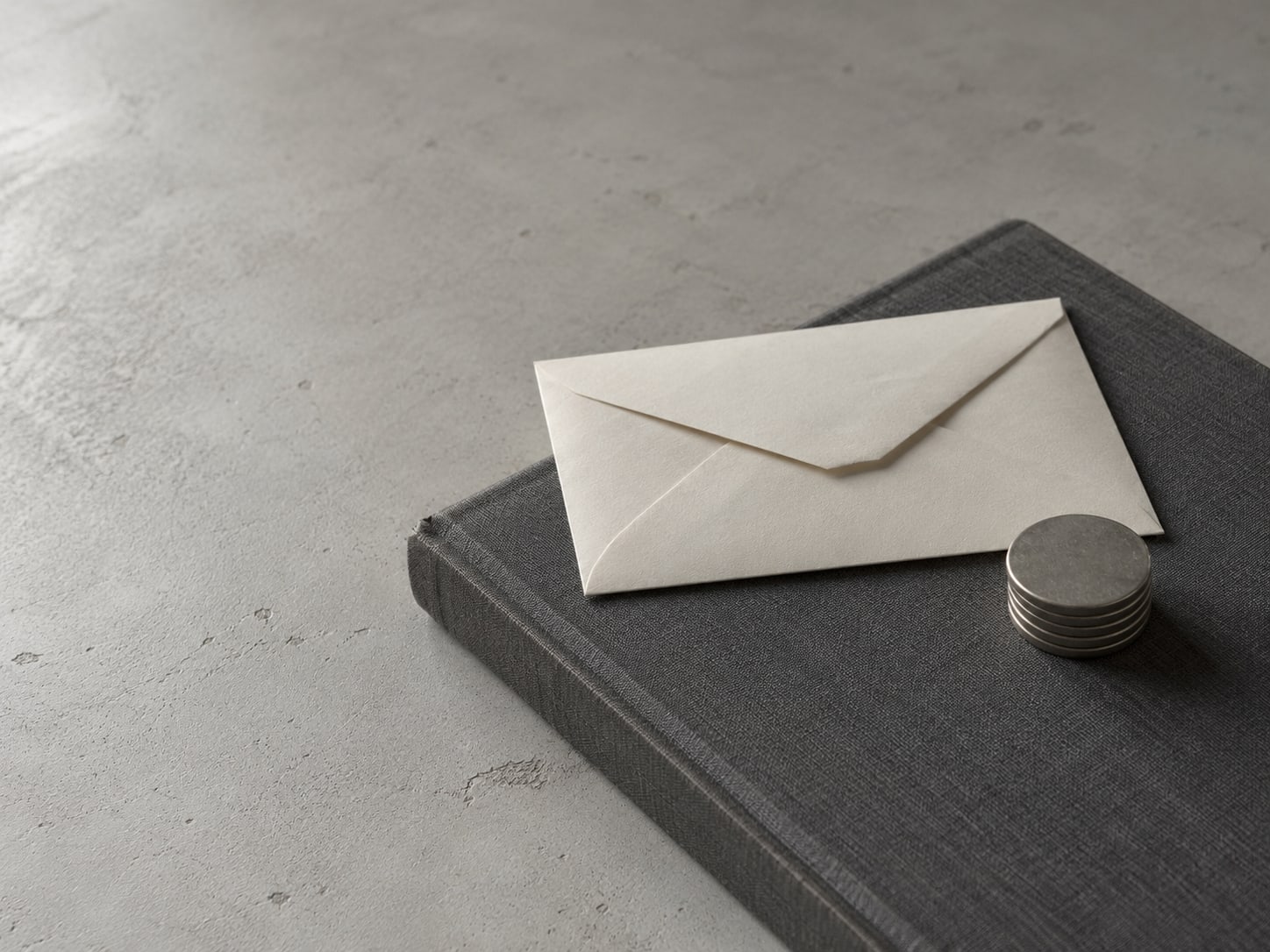 A sealed envelope and a short stack of coins on a closed ledger book.
