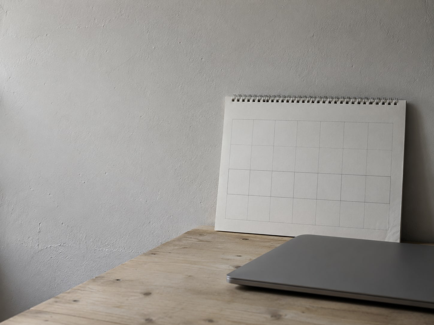 A paper wall calendar with two blank weeks outlined in pencil beside a closed laptop.