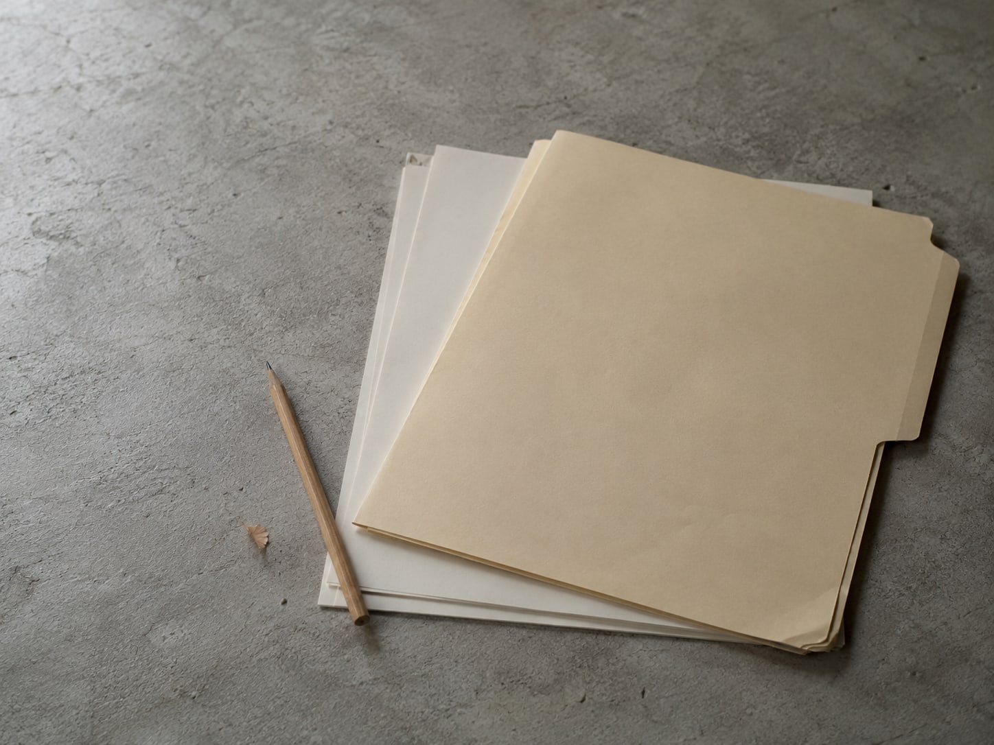 A closed manila folder and a sharpened pencil on a desk beside a stack of blank paper.
