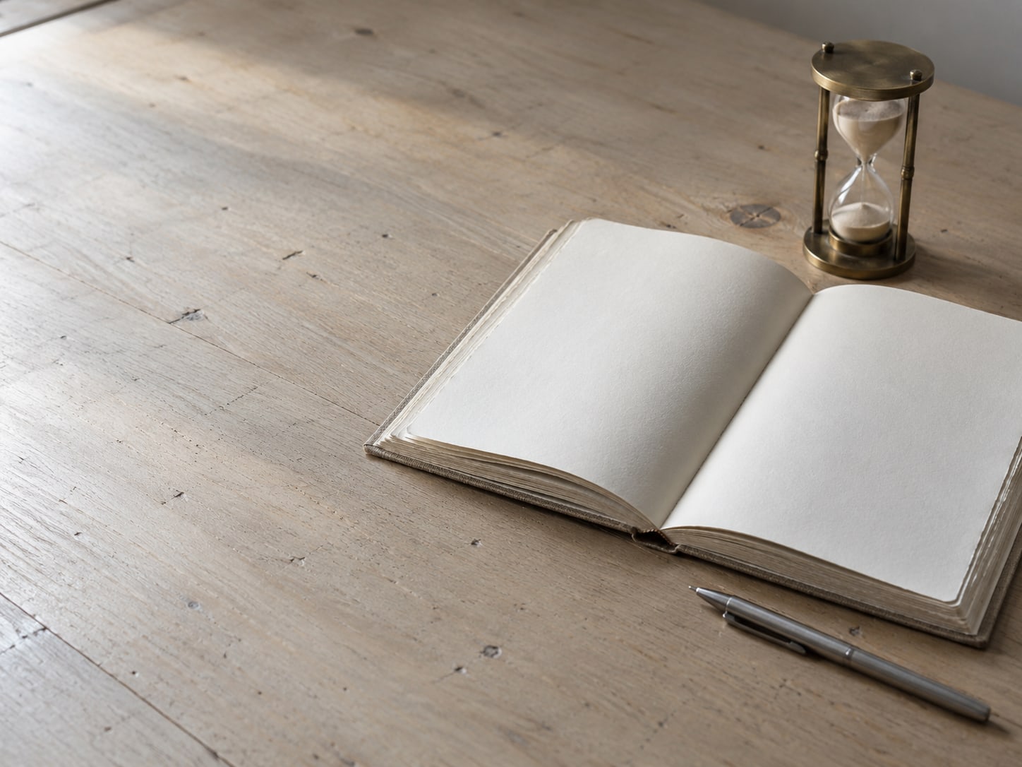 A paper ledger book lying open beside a small brass hourglass and a pen on a plain desk.