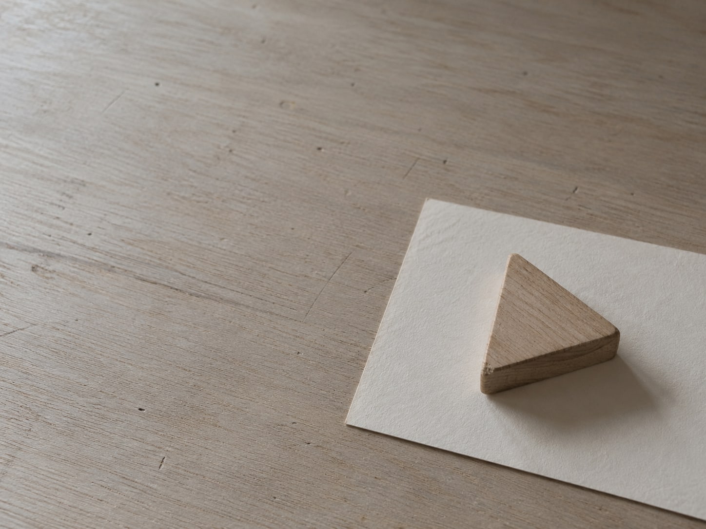 A small wooden block shaped like a play button resting on a blank cream card on a pale desk.