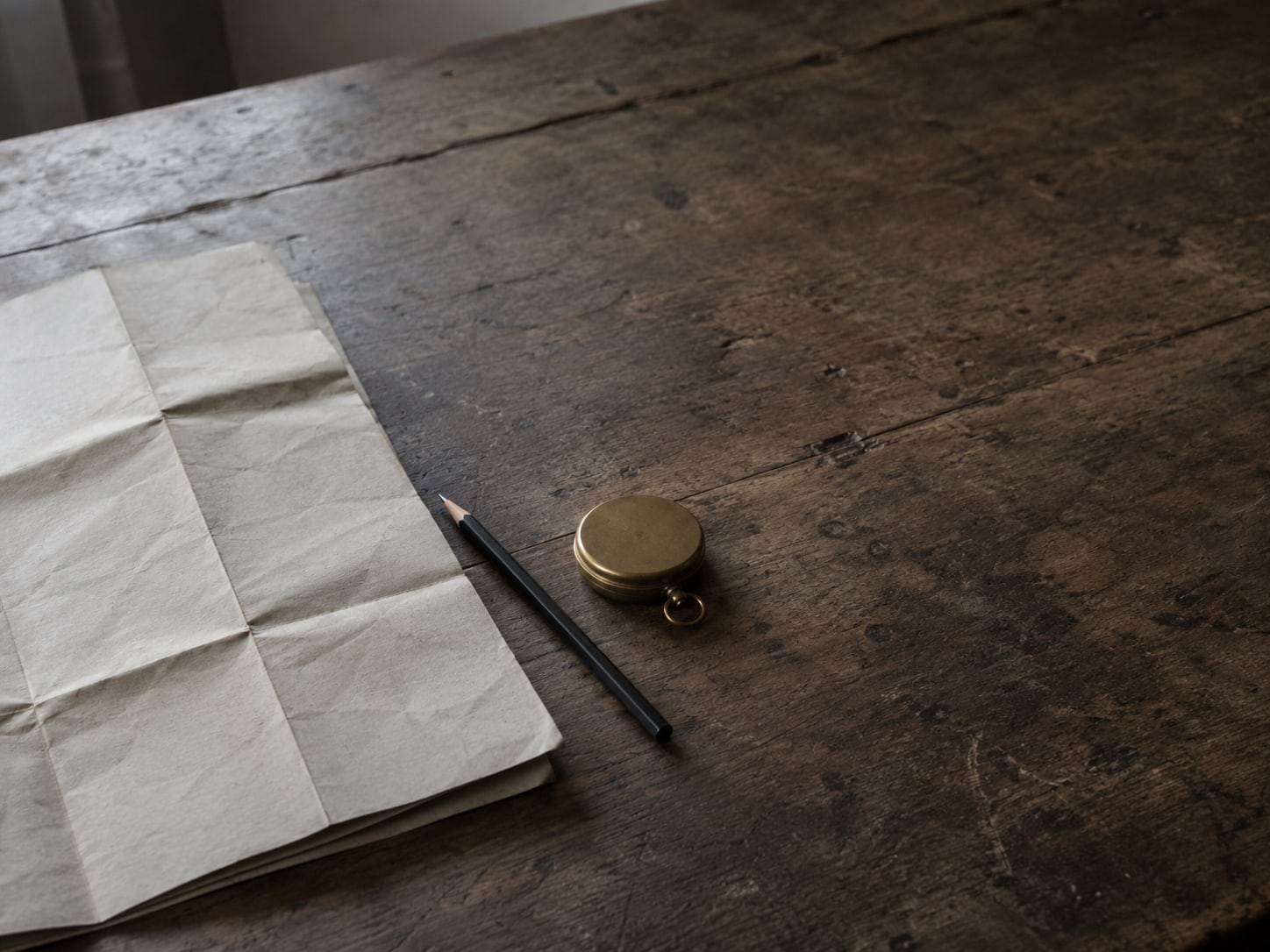 Un mapa de calles de papel doblado, un lápiz y una pequeña brújula de latón sobre una mesa de madera gastada.