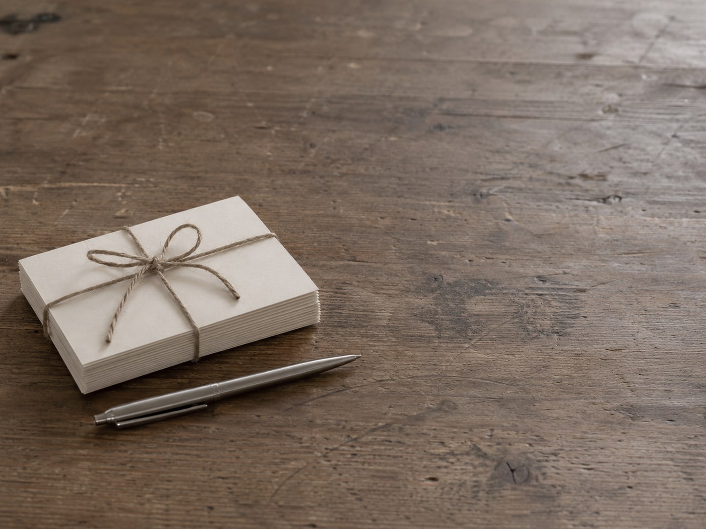 A small stack of blank thank-you cards tied with twine, with a pen lying beside them on a kitchen table.