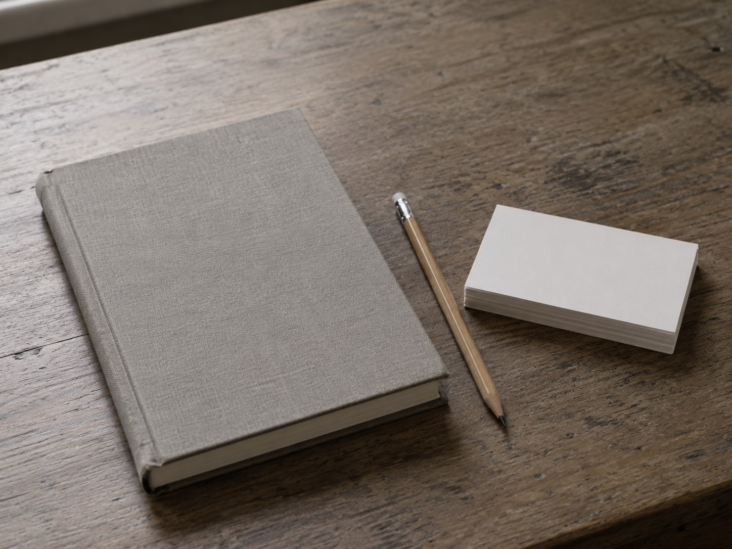 A closed notebook and a pencil lying beside a neat stack of blank index cards on a wooden desk.
