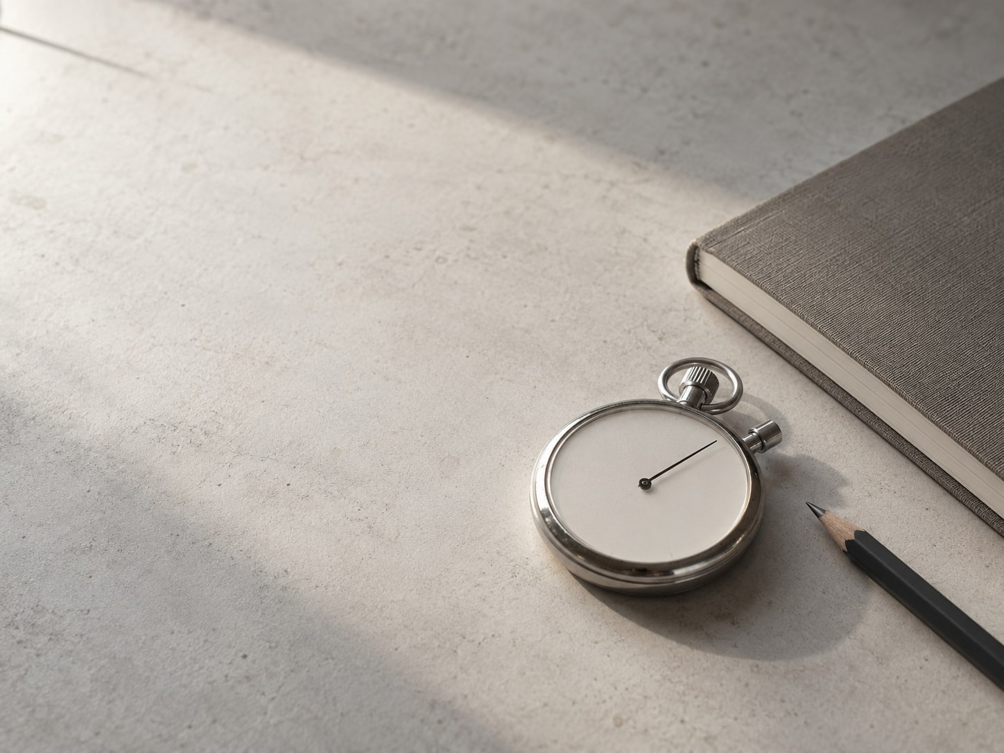 A stopwatch lying on a clean desk beside a closed notebook and a pencil.