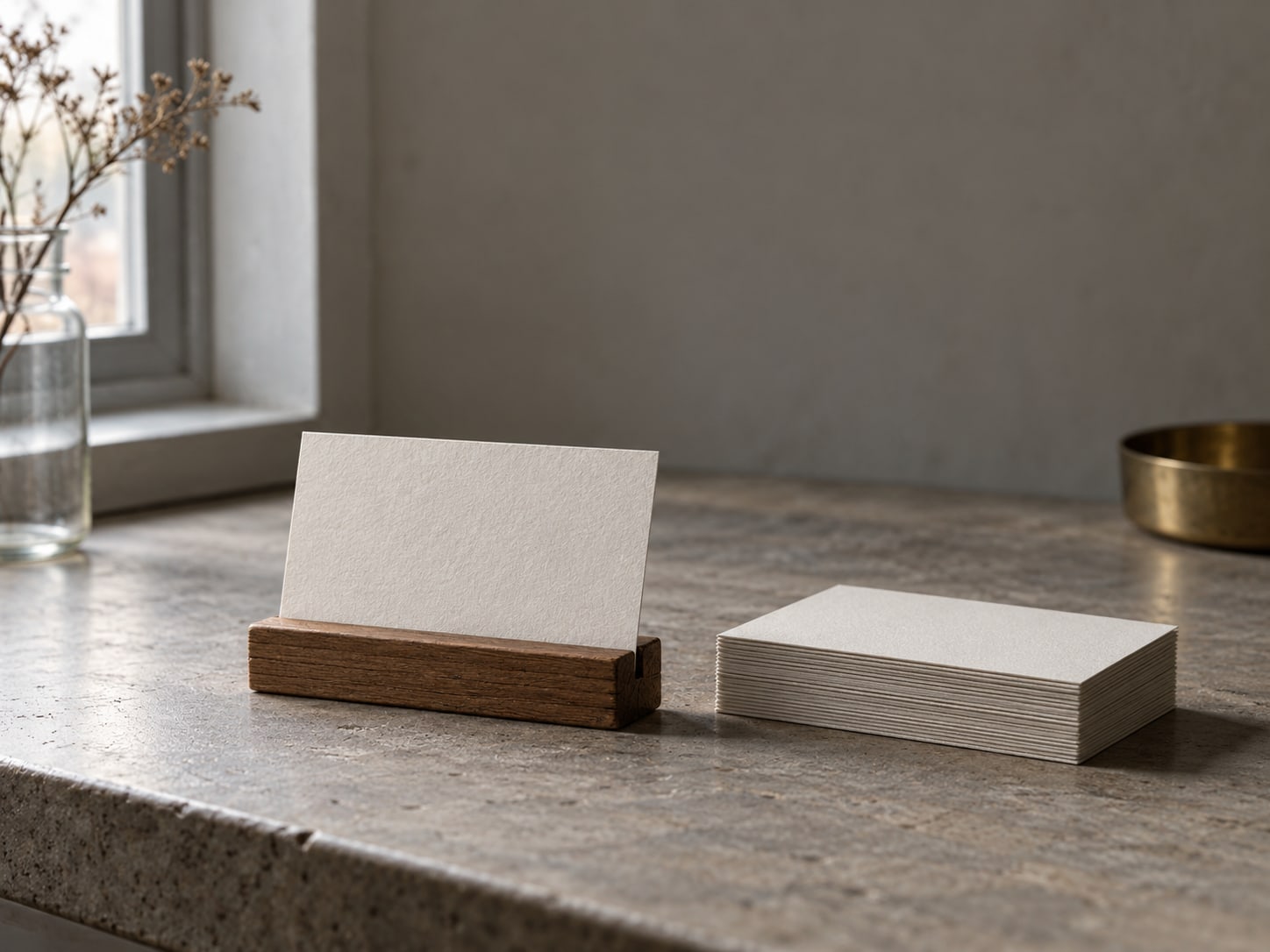 A small stand holding a blank printed card beside a stack of unmarked cards on a countertop.