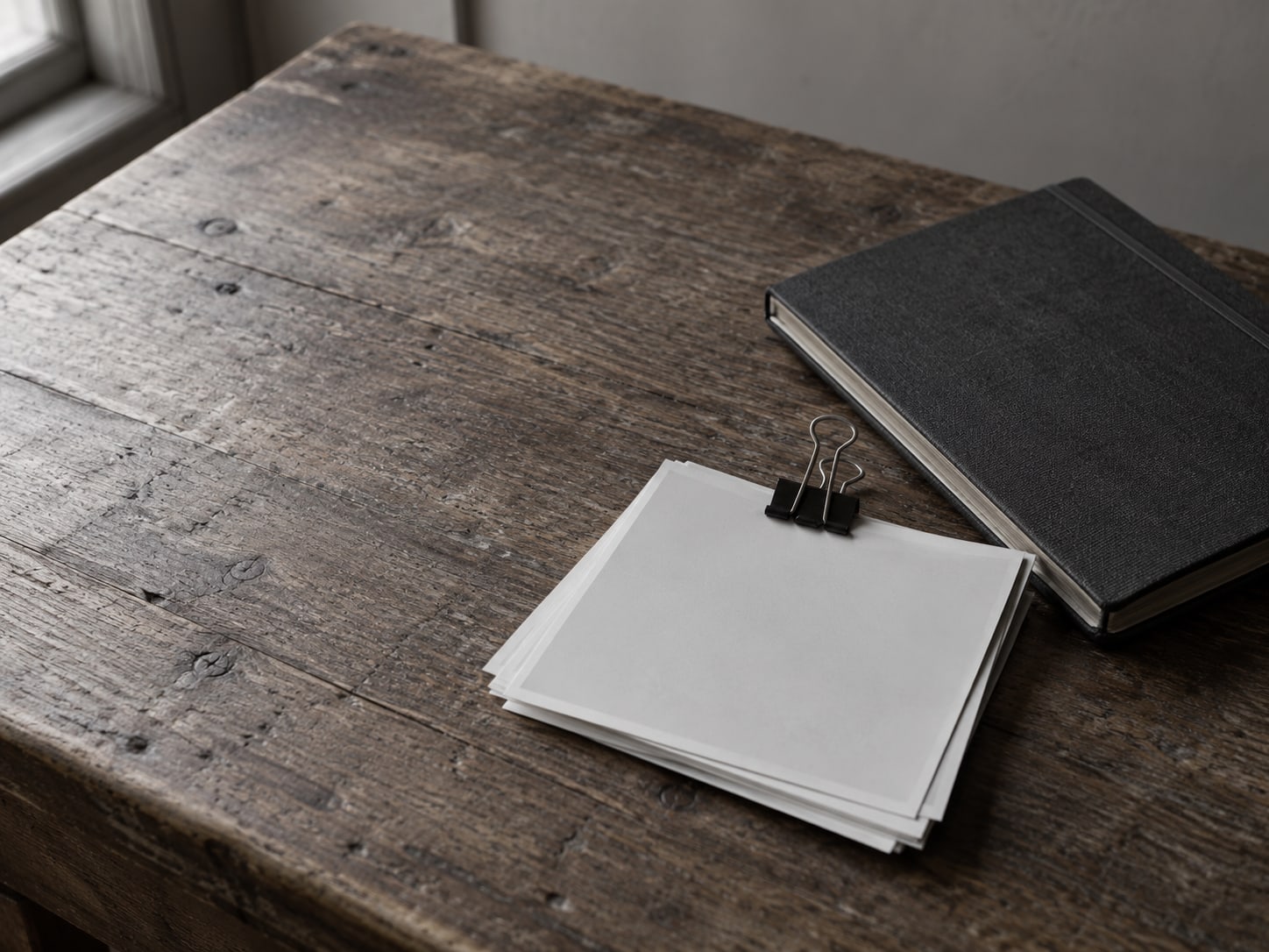 A small stack of printed sample photos held together with a binder clip beside a plain notebook on a wooden table.