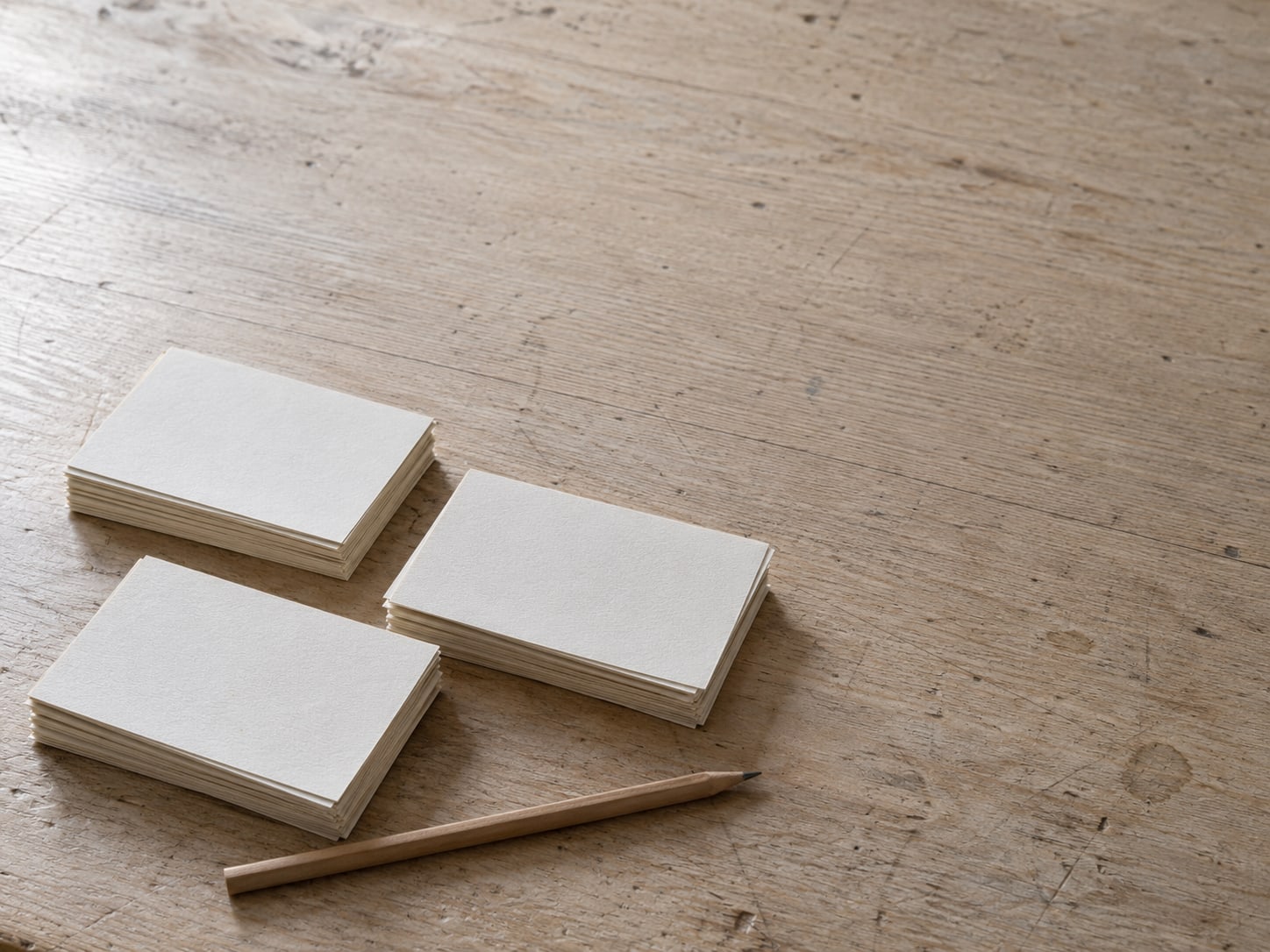 A small stack of blank index cards sorted into three neat piles beside a pencil on a desk.