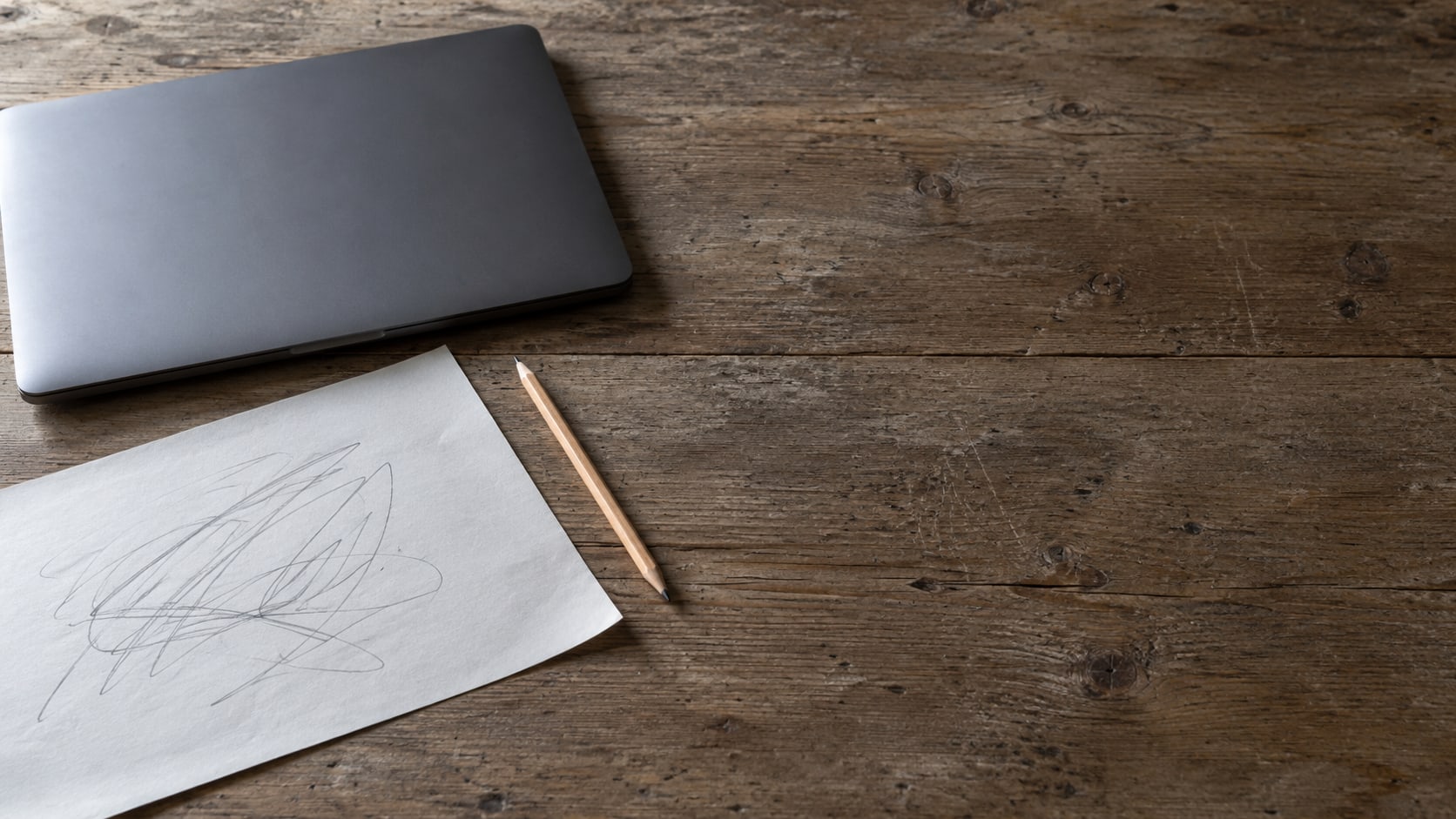 A printed page with pencil marks, a pencil and a closed laptop on a wooden desk.
