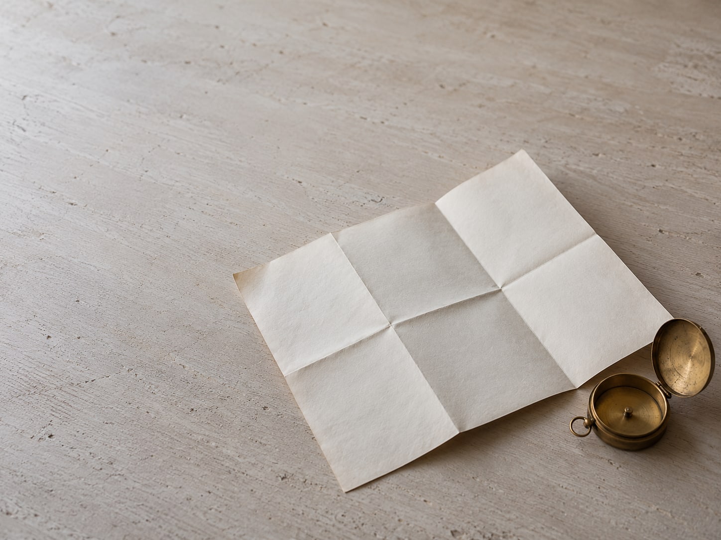 A single folded paper map lying flat on a plain table beside a small brass compass.