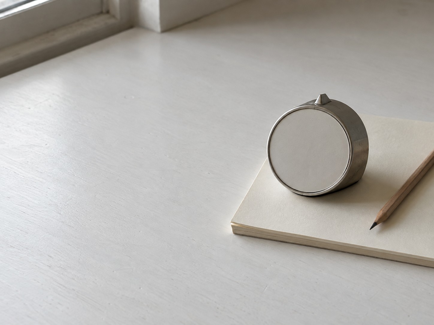 A blank notepad with faint pencil columns, a pencil and a closed laptop on a kitchen table.